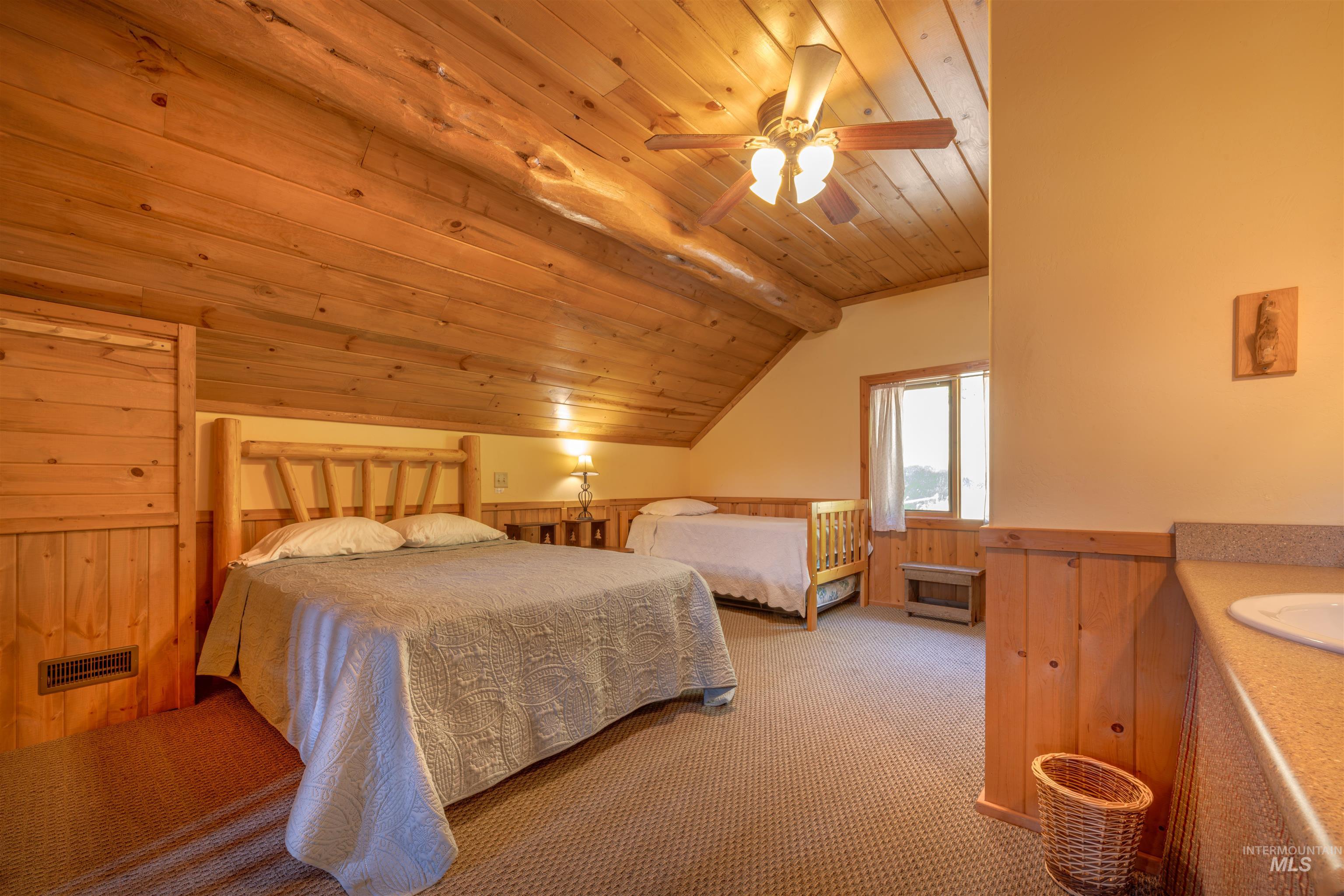 Carpeted bedroom featuring lofted ceiling, wooden ceiling, a wainscoted wall, wood walls, and a ceiling fan