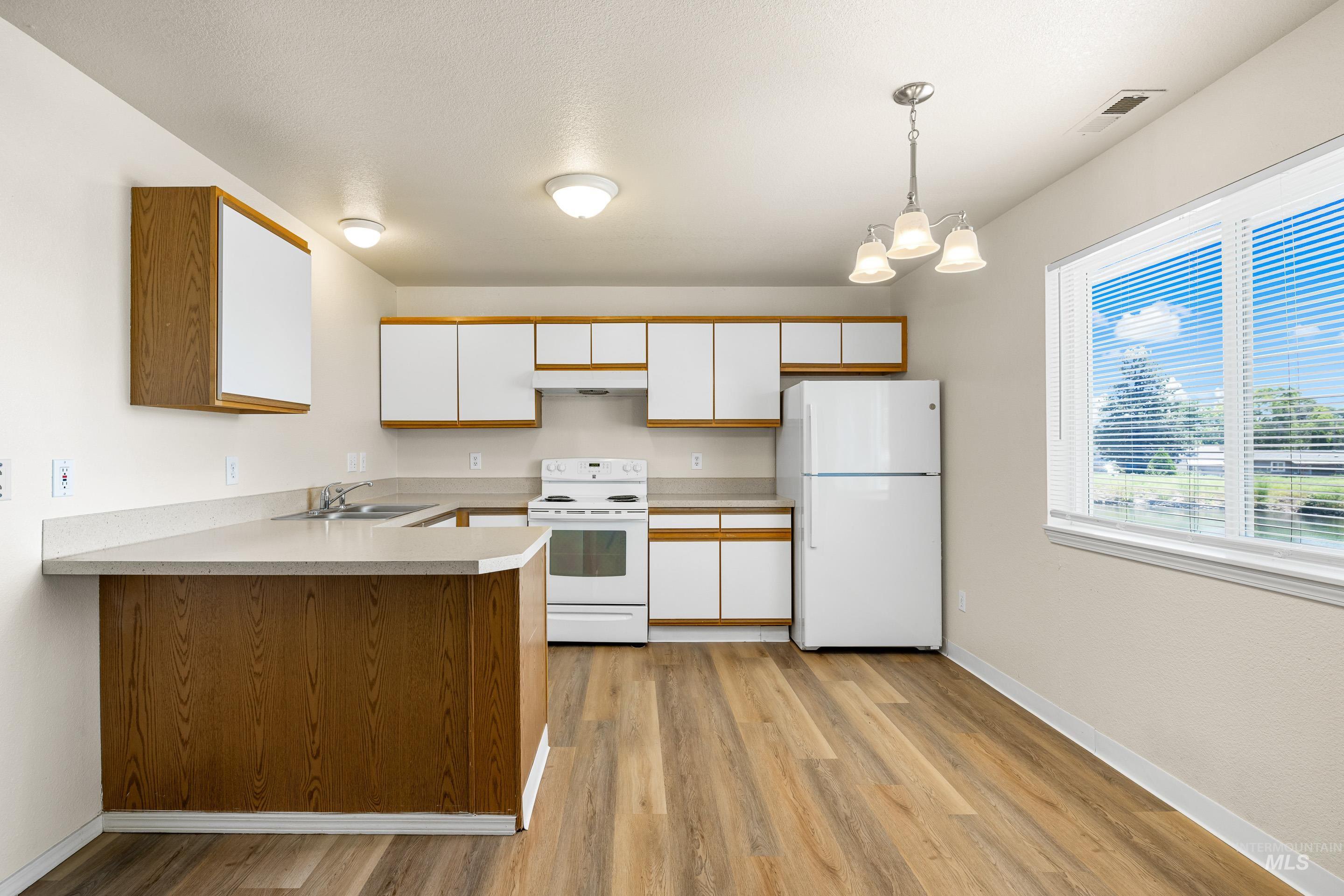 Kitchen featuring white appliances, light wood finished floors, white cabinetry, a peninsula, and light countertops