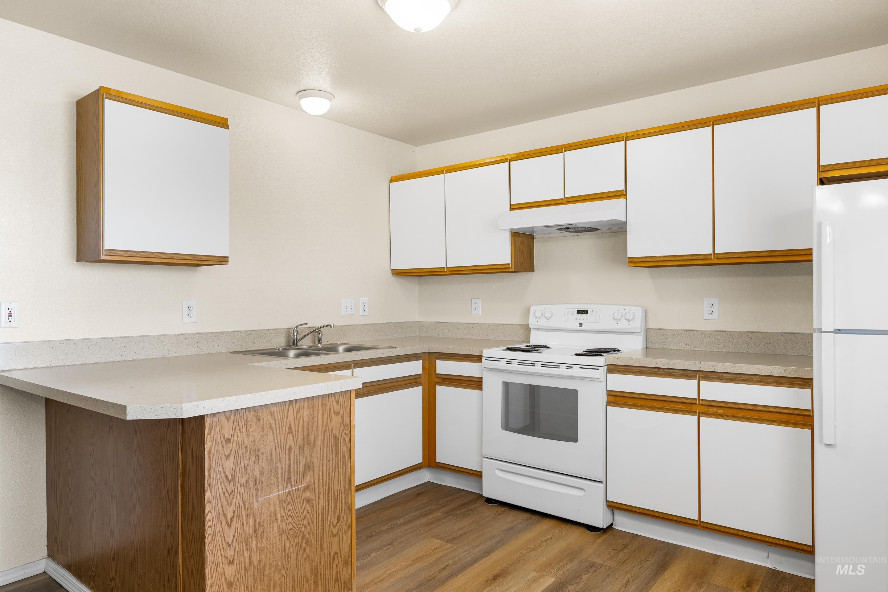 Kitchen featuring white appliances, a peninsula, white cabinetry, and light wood-style floors