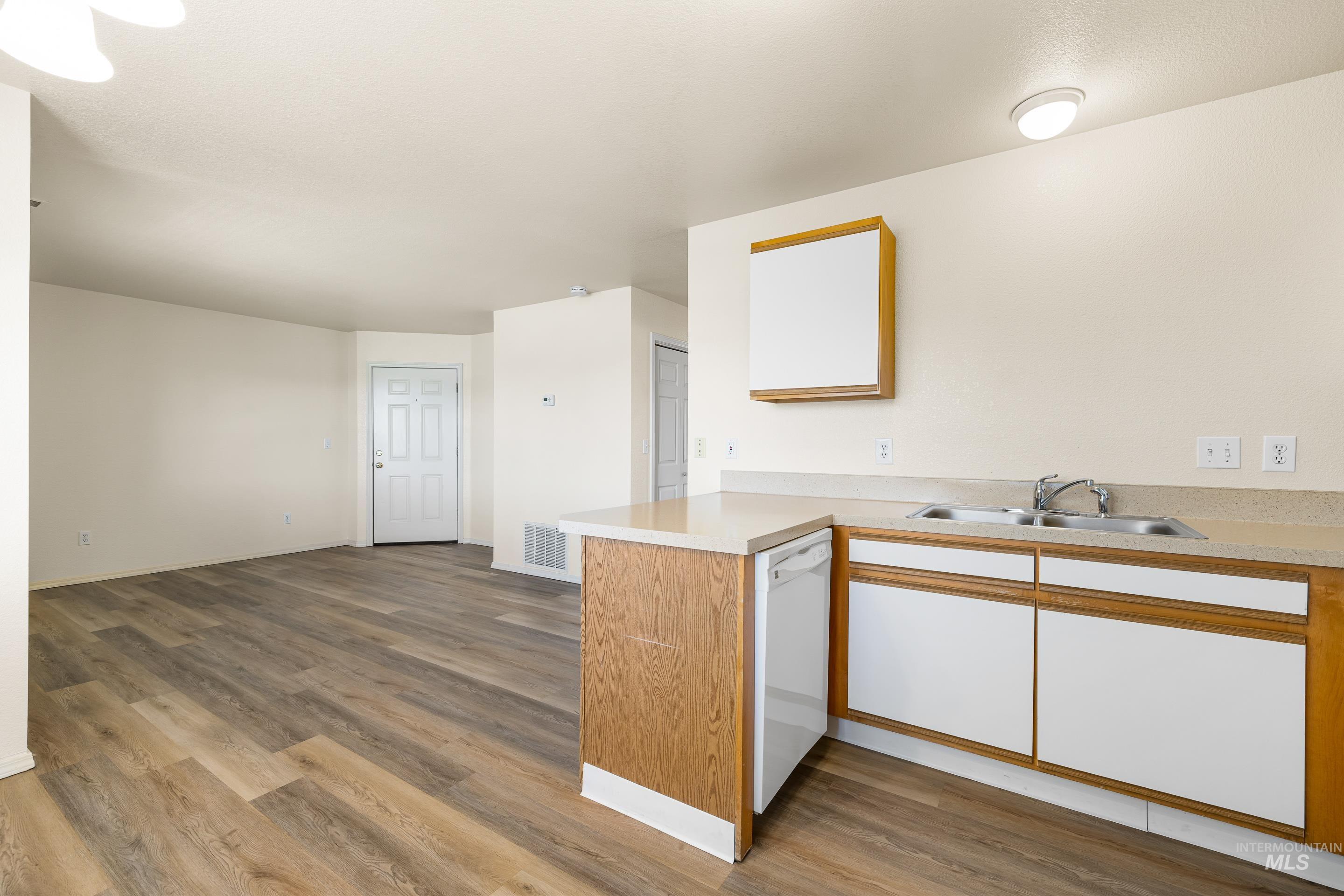 Kitchen featuring dishwasher, wood finished floors, light countertops, and a peninsula