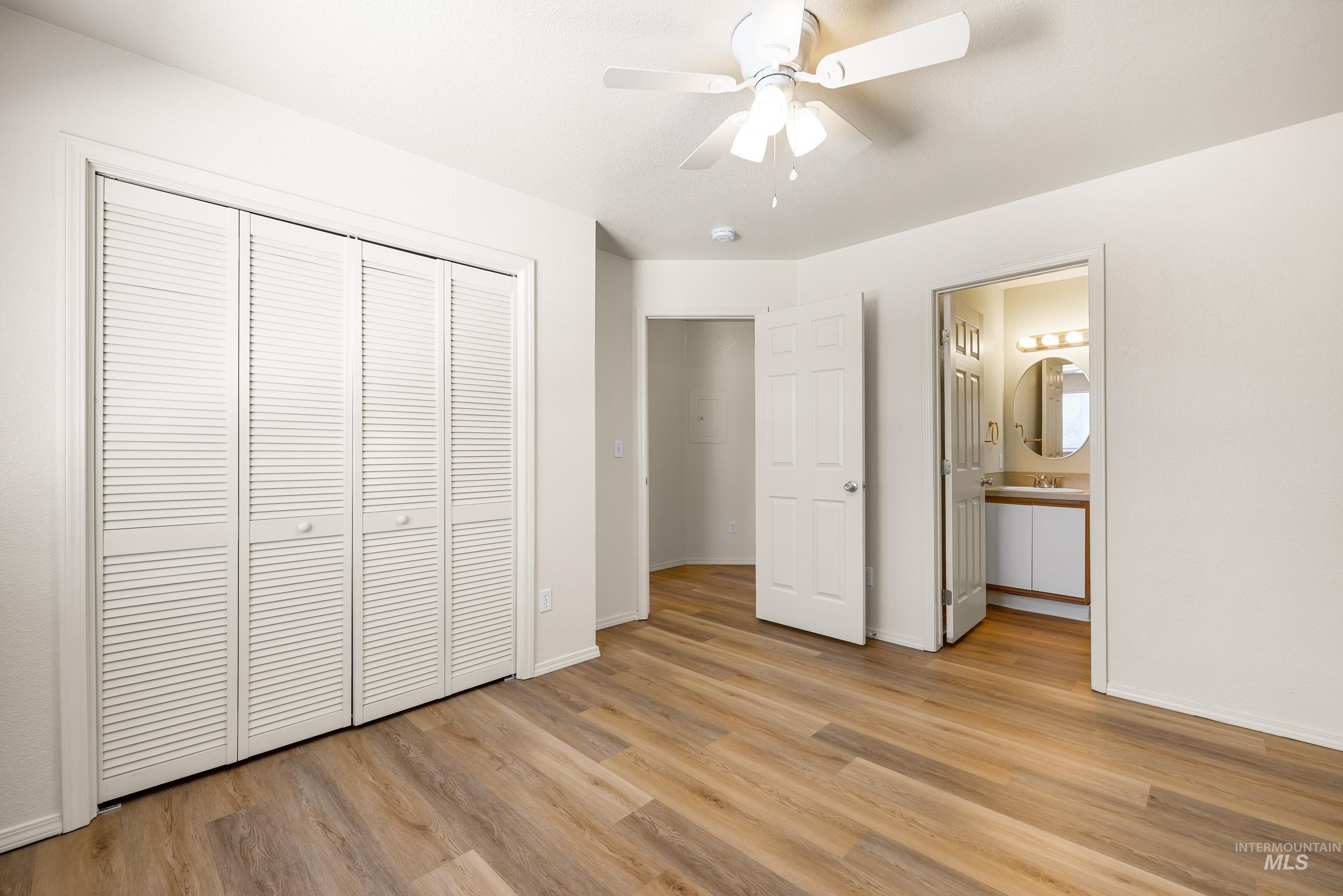 Unfurnished bedroom featuring light wood-style flooring, a closet, connected bathroom, and a ceiling fan