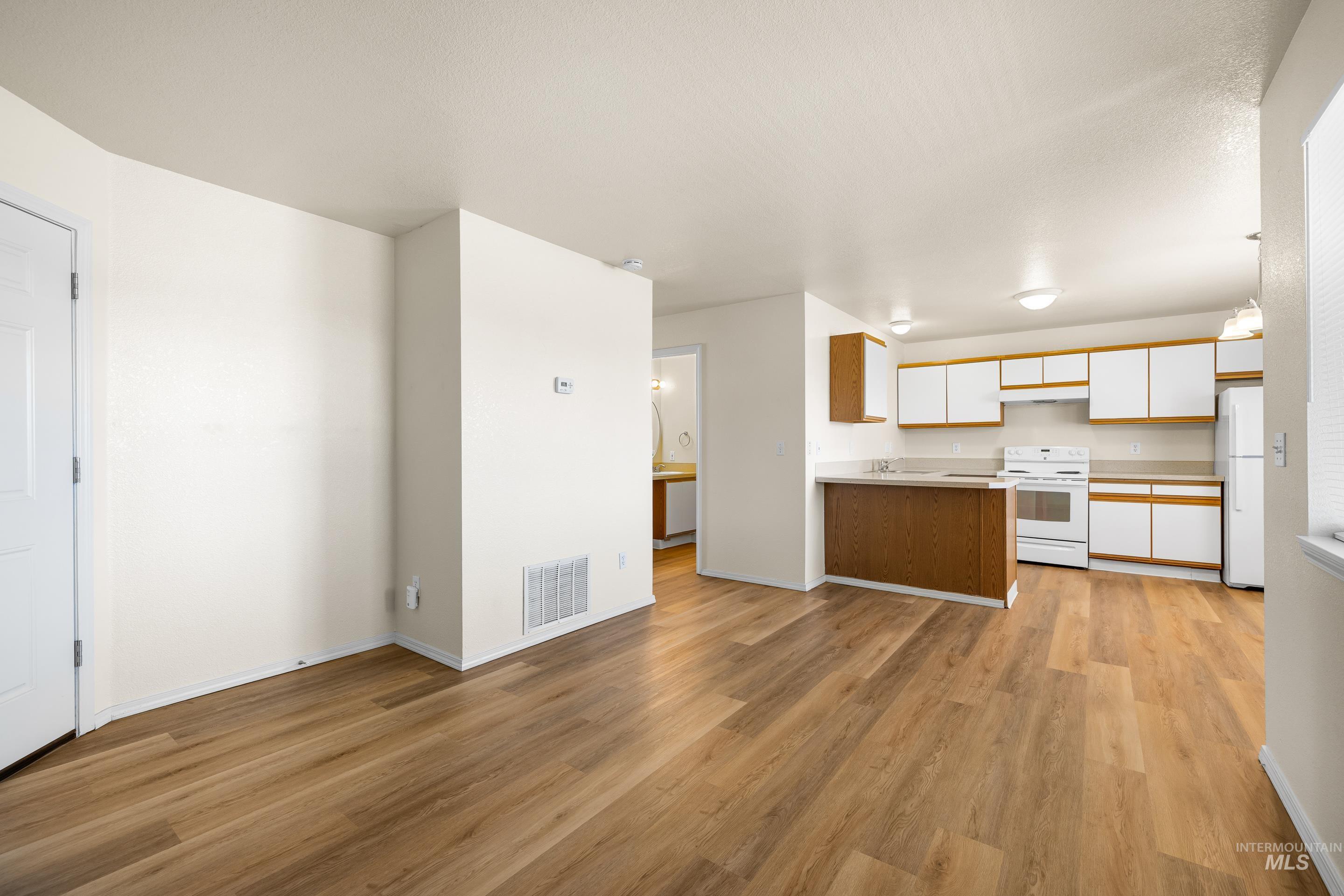 Kitchen featuring white appliances, white cabinets, light wood-style flooring, light countertops, and open floor plan