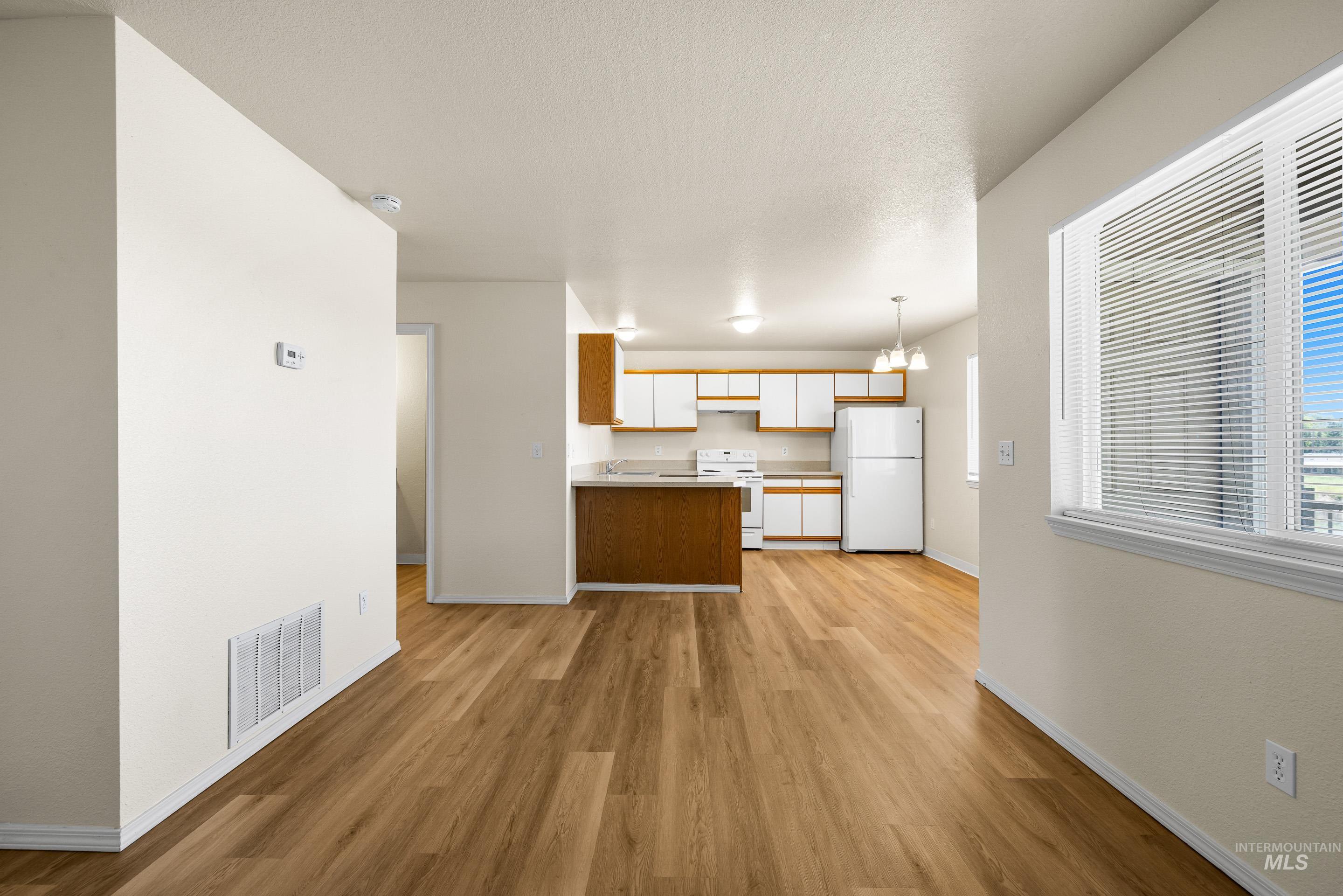 Kitchen featuring white appliances, light wood-style floors, light countertops, a peninsula, and decorative light fixtures
