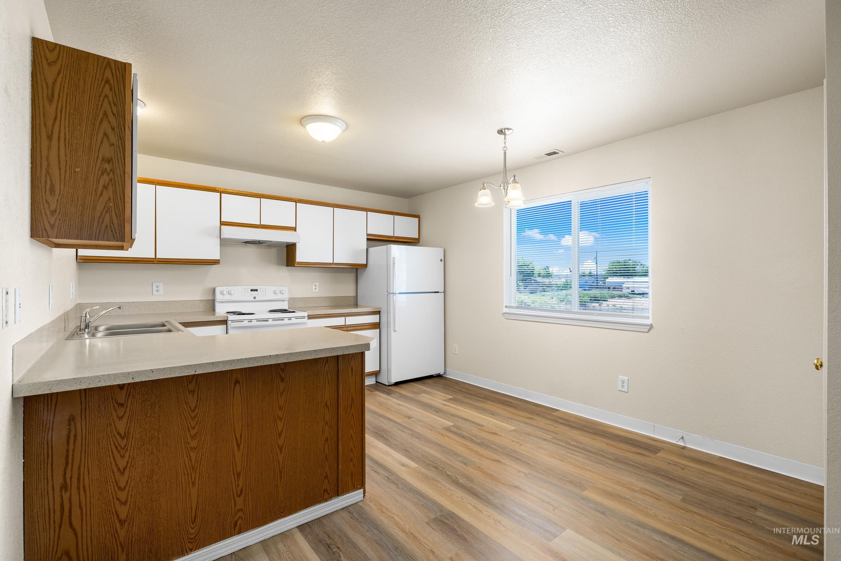 Kitchen featuring white appliances, under cabinet range hood, a peninsula, light wood-style flooring, and light countertops