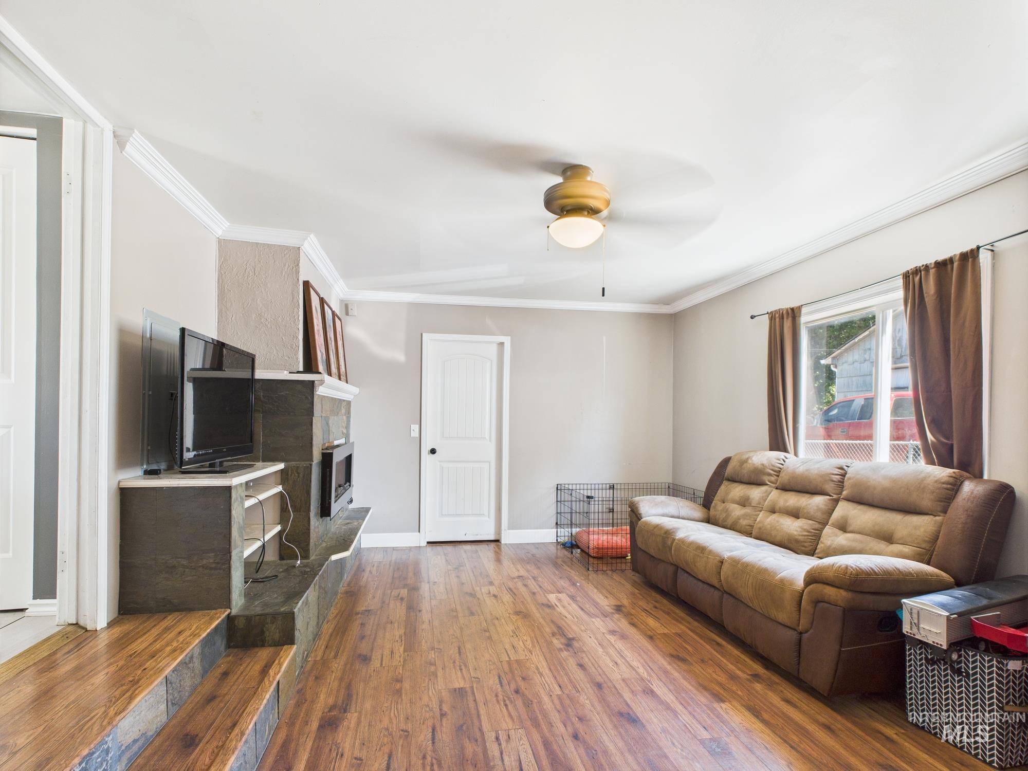 Living area with dark wood-style floors, ceiling fan, a tiled fireplace, and ornamental molding