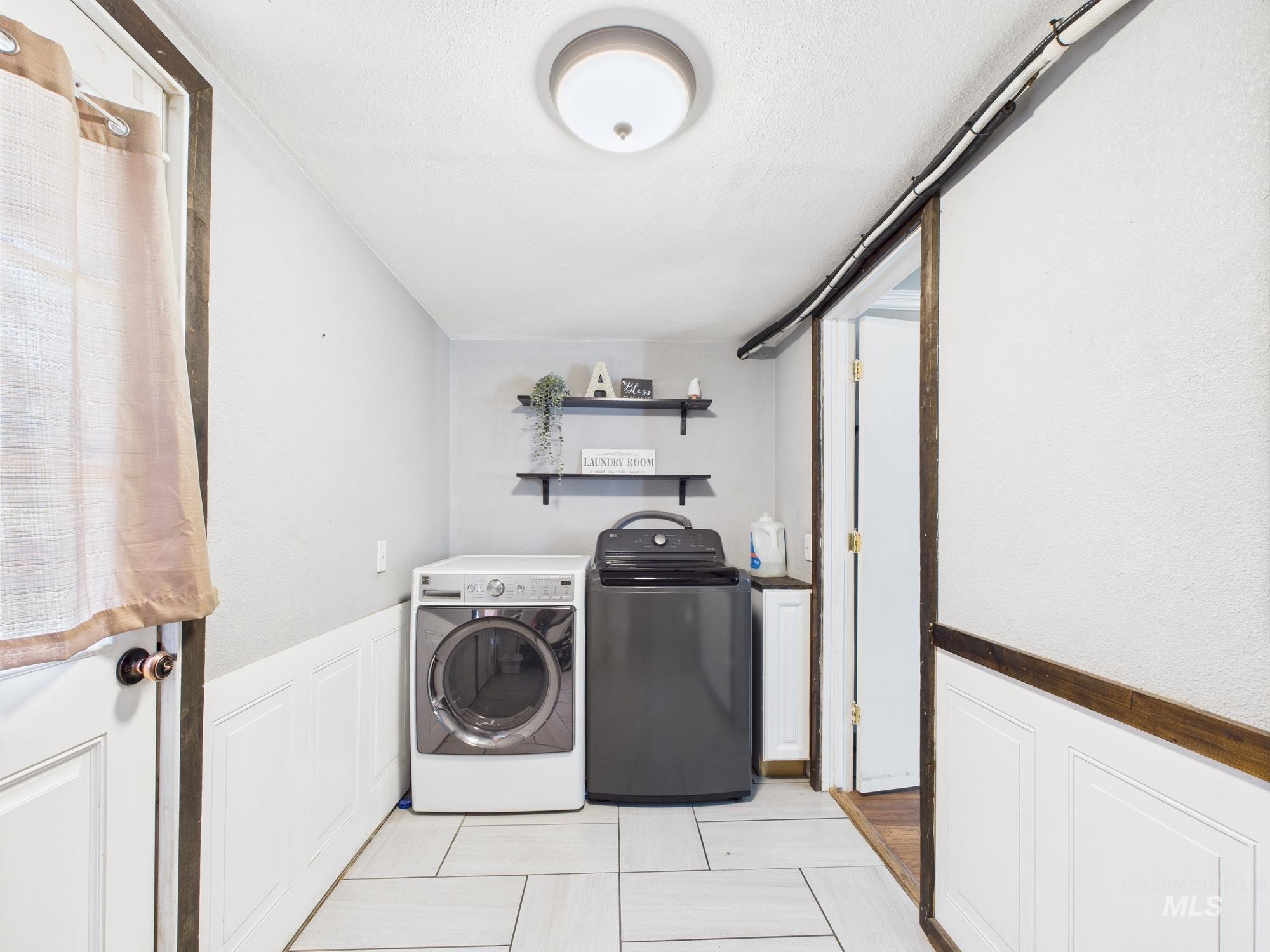 Laundry area featuring separate washer and dryer, wainscoting, and light tile patterned flooring