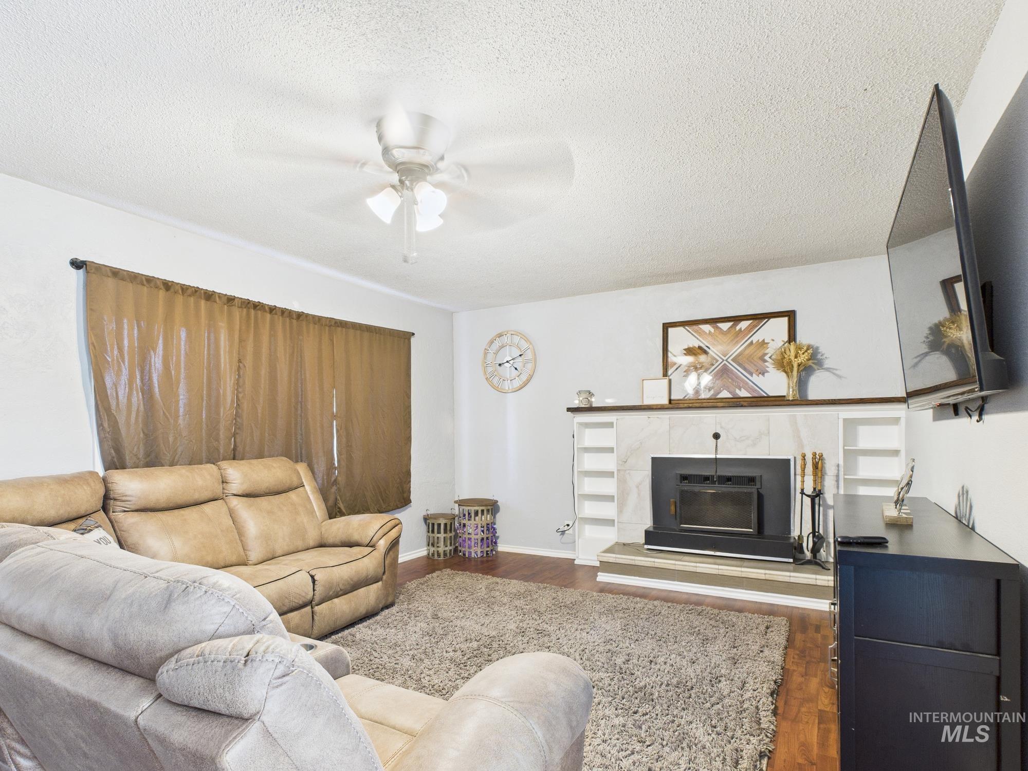 Living area featuring wood finished floors, ceiling fan, a textured ceiling, and a tile fireplace