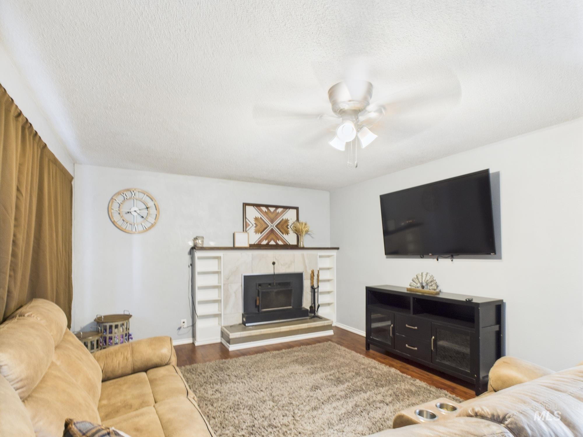 Living room with ceiling fan, wood finished floors, a textured ceiling, and a glass covered fireplace