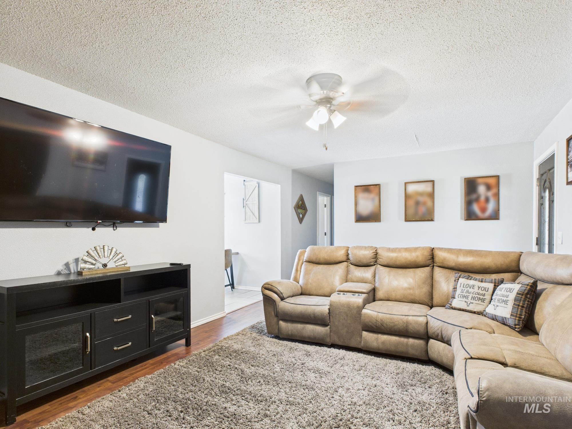 Living room with a ceiling fan, dark wood-style flooring, and a textured ceiling
