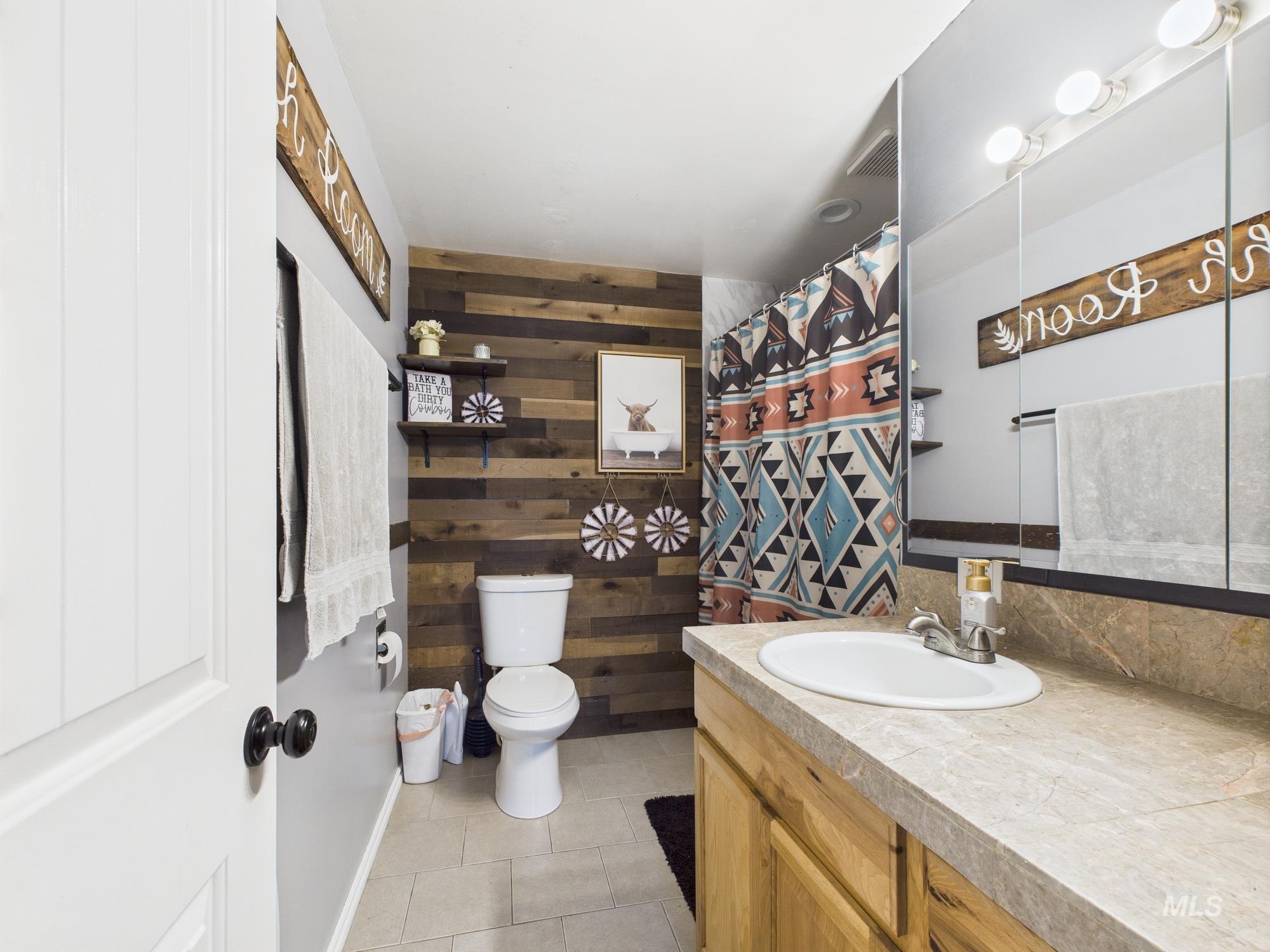 Bathroom with vanity, wooden walls, tile patterned flooring, and a shower with shower curtain
