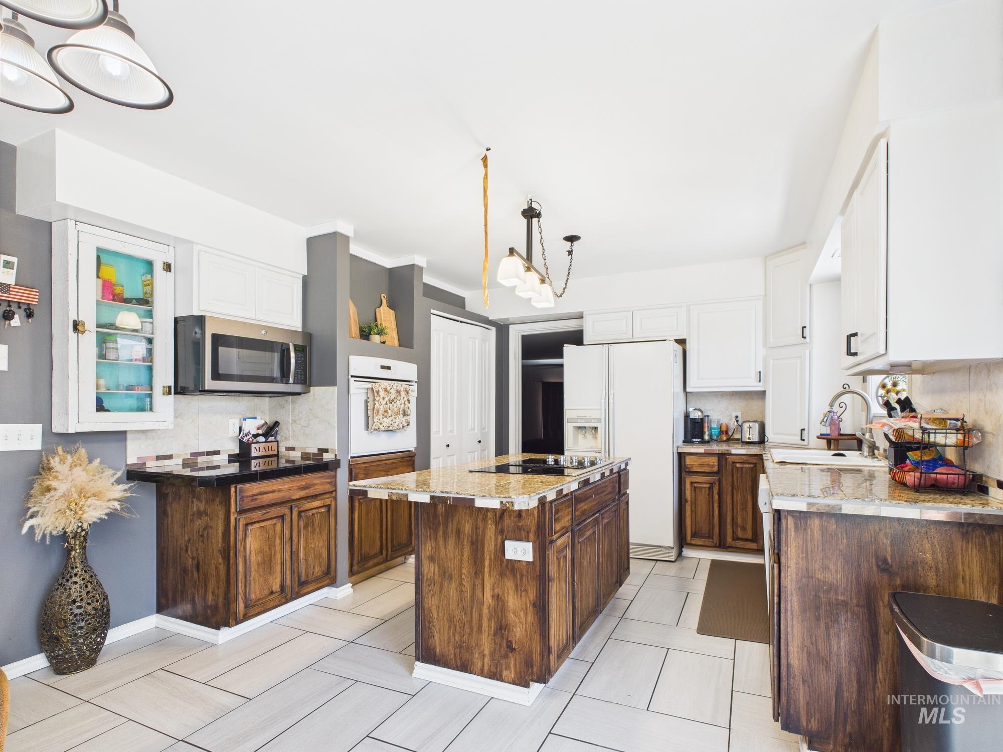 Kitchen with white appliances, tasteful backsplash, a center island, white cabinetry, and decorative light fixtures