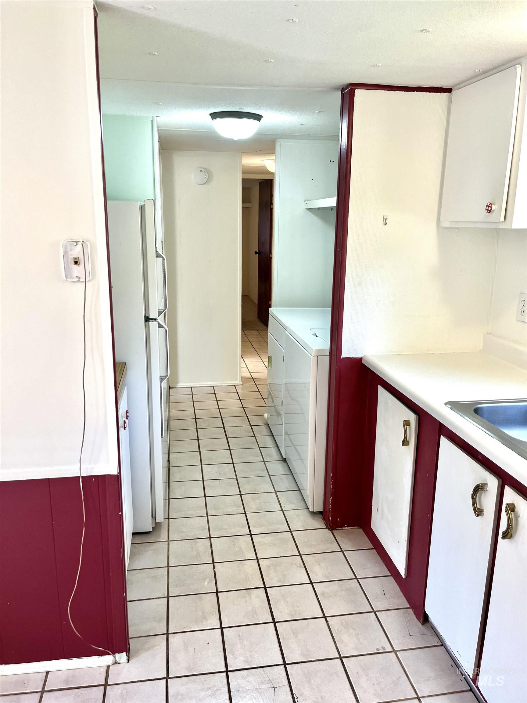 Kitchen featuring separate washer and dryer, freestanding refrigerator, light tile patterned floors, white cabinets, and light countertops