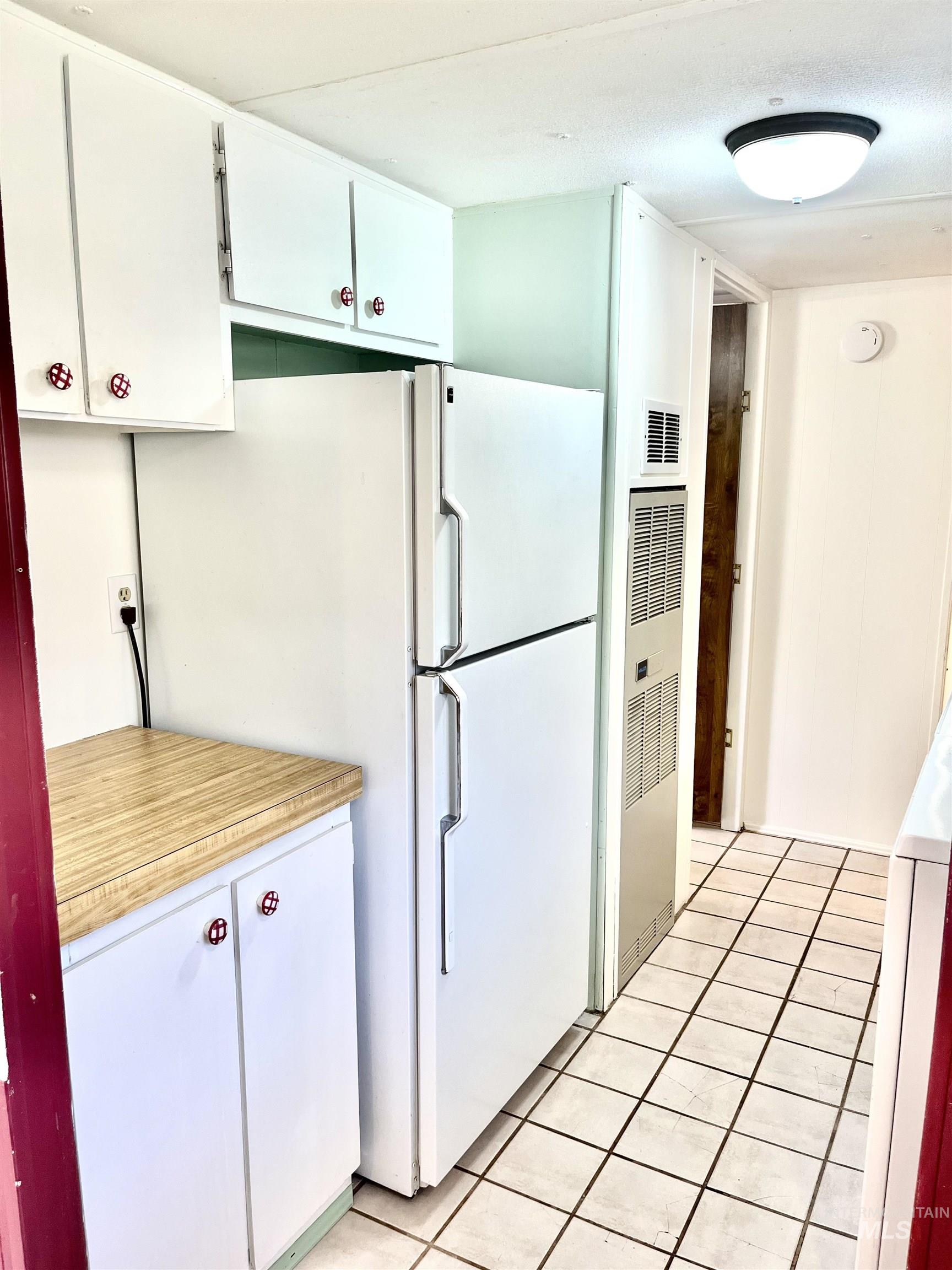 Kitchen with light tile patterned flooring, light countertops, white cabinets, and freestanding refrigerator