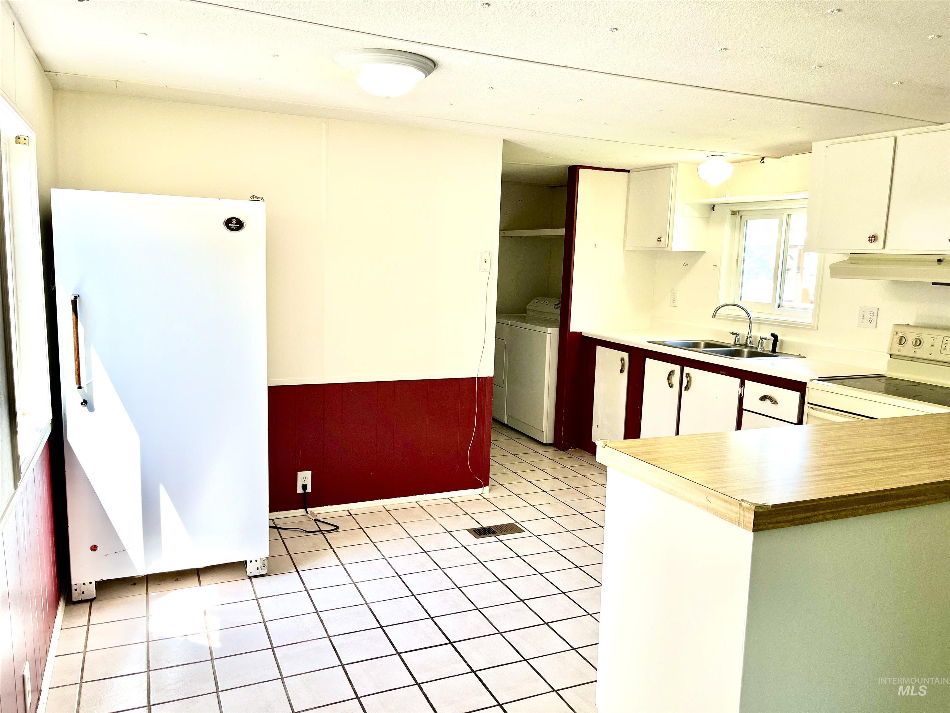 Kitchen featuring white appliances, under cabinet range hood, washer and dryer, white cabinetry, and light countertops