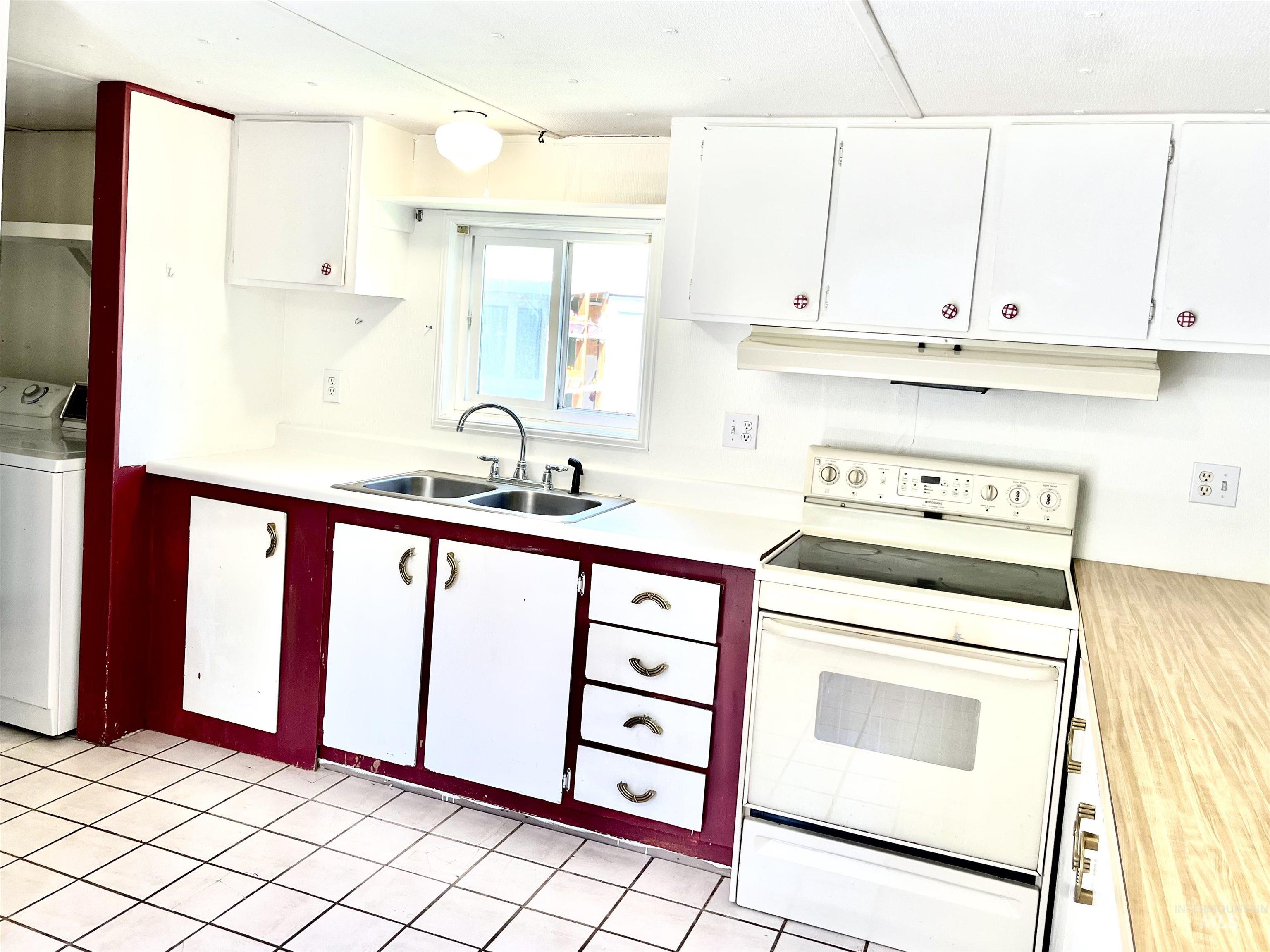 Kitchen with white range with electric cooktop, washer / clothes dryer, under cabinet range hood, light countertops, and white cabinets