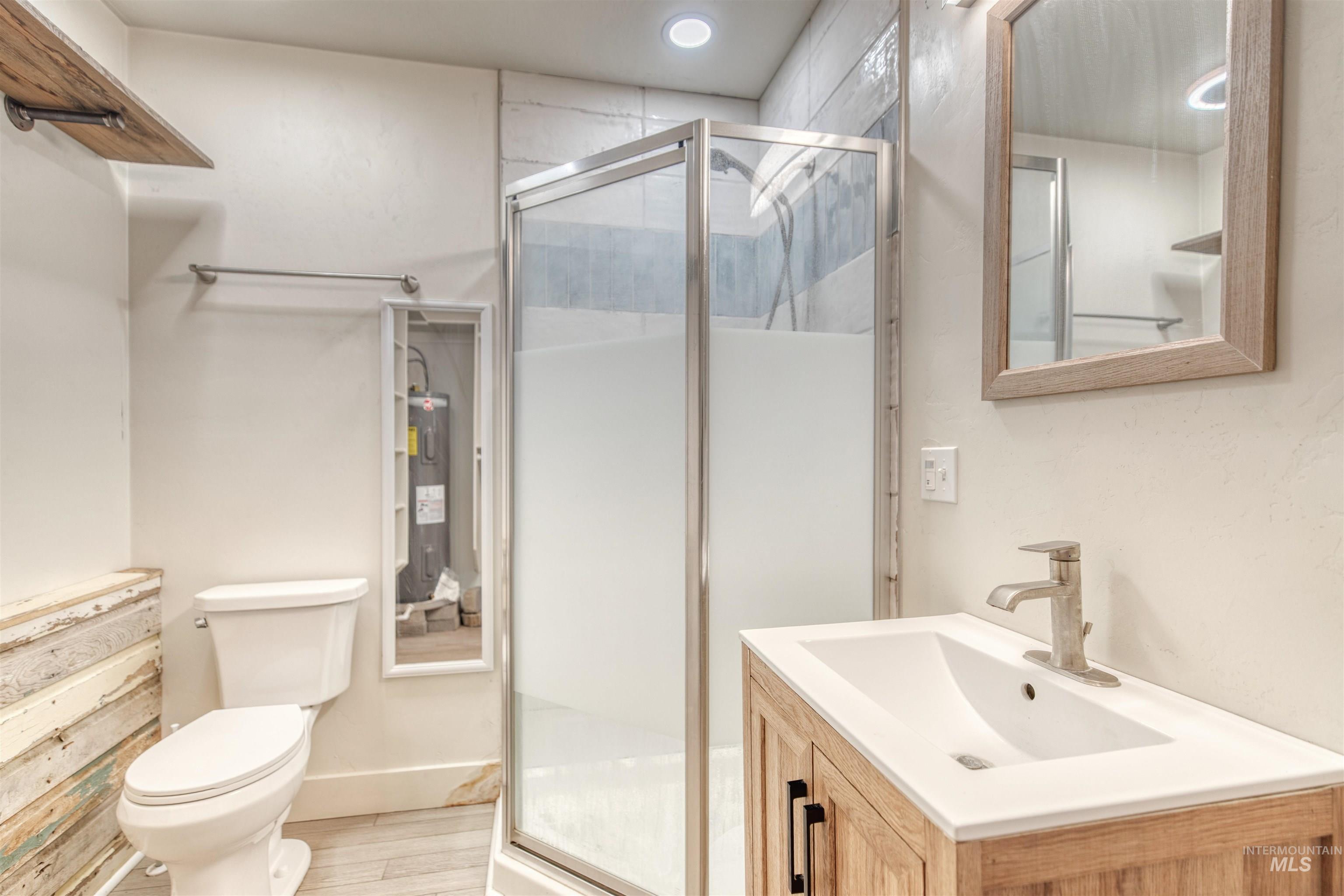 Full bath with water heater, vanity, a stall shower, wood finished floors, and recessed lighting