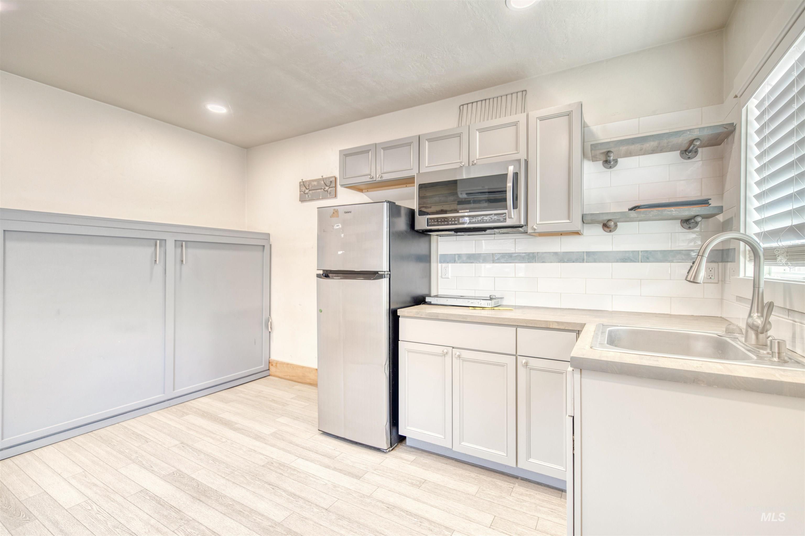 Kitchen with freestanding refrigerator, stainless steel microwave, open shelves, light wood-type flooring, and recessed lighting
