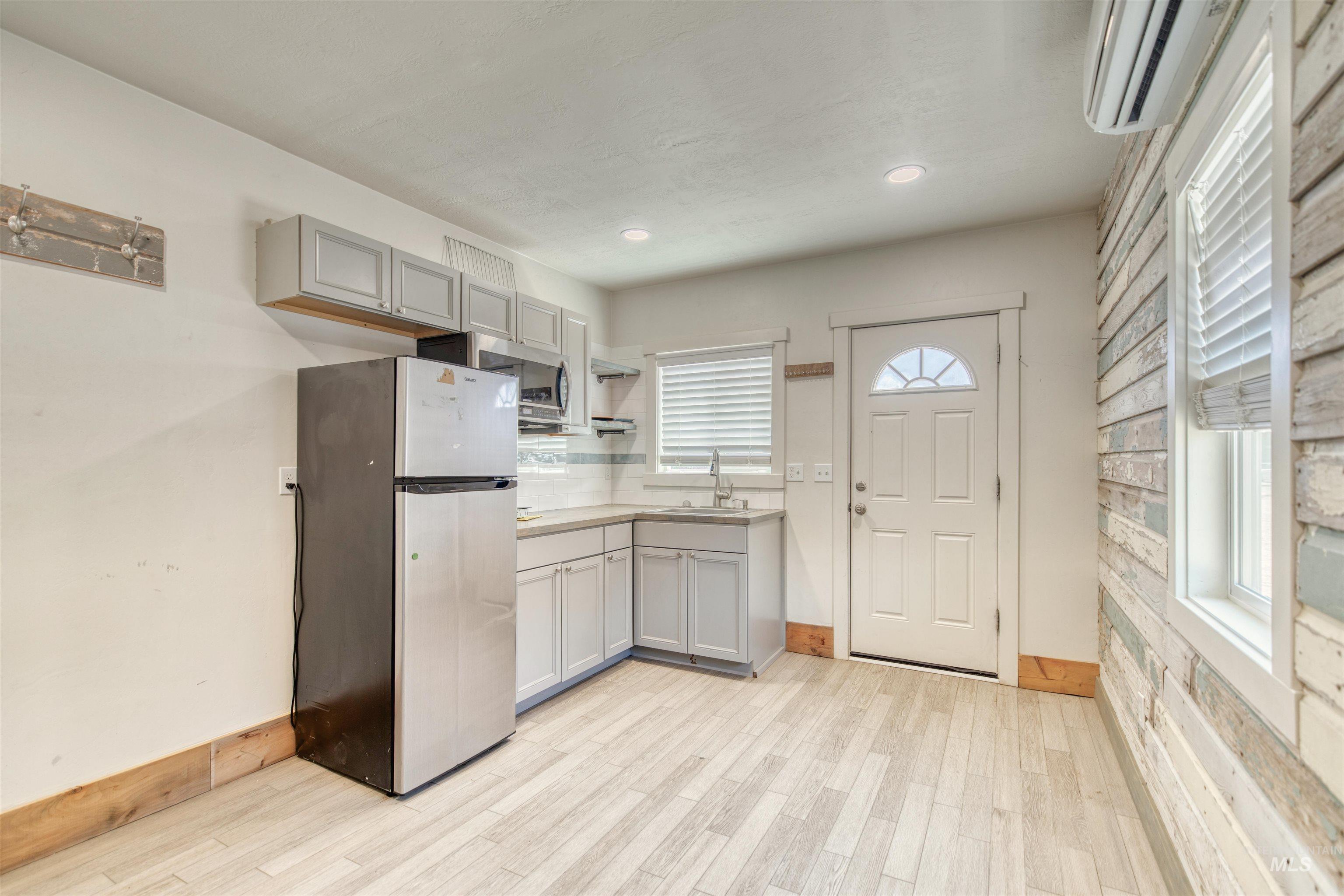 Kitchen with appliances with stainless steel finishes, gray cabinets, an AC wall unit, light wood-style floors, and recessed lighting