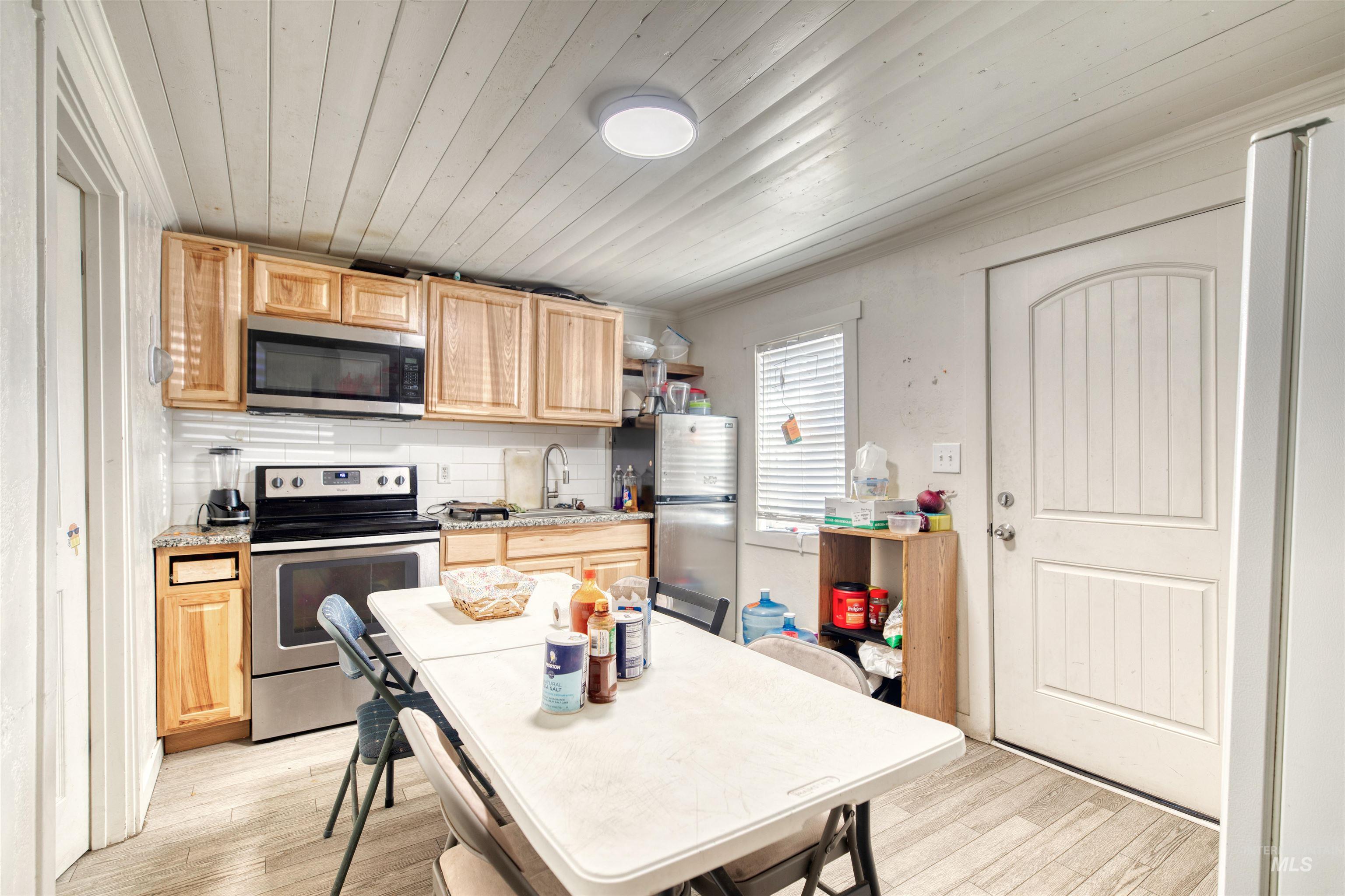 Kitchen with stainless steel appliances, light brown cabinets, light wood-type flooring, backsplash, and wood ceiling