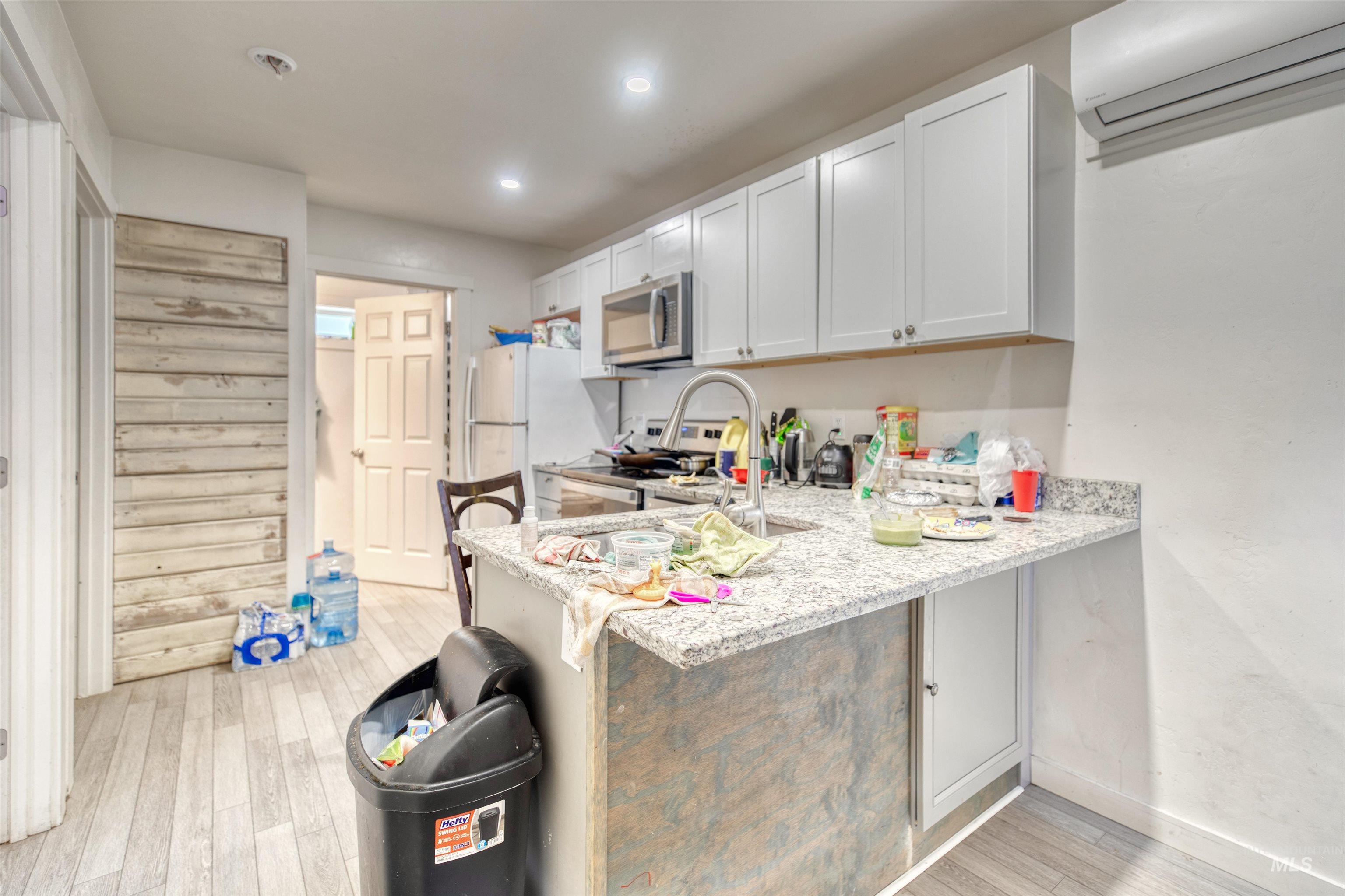 Kitchen with stainless steel appliances, a wall mounted AC, light wood-style floors, a breakfast bar area, and light stone countertops