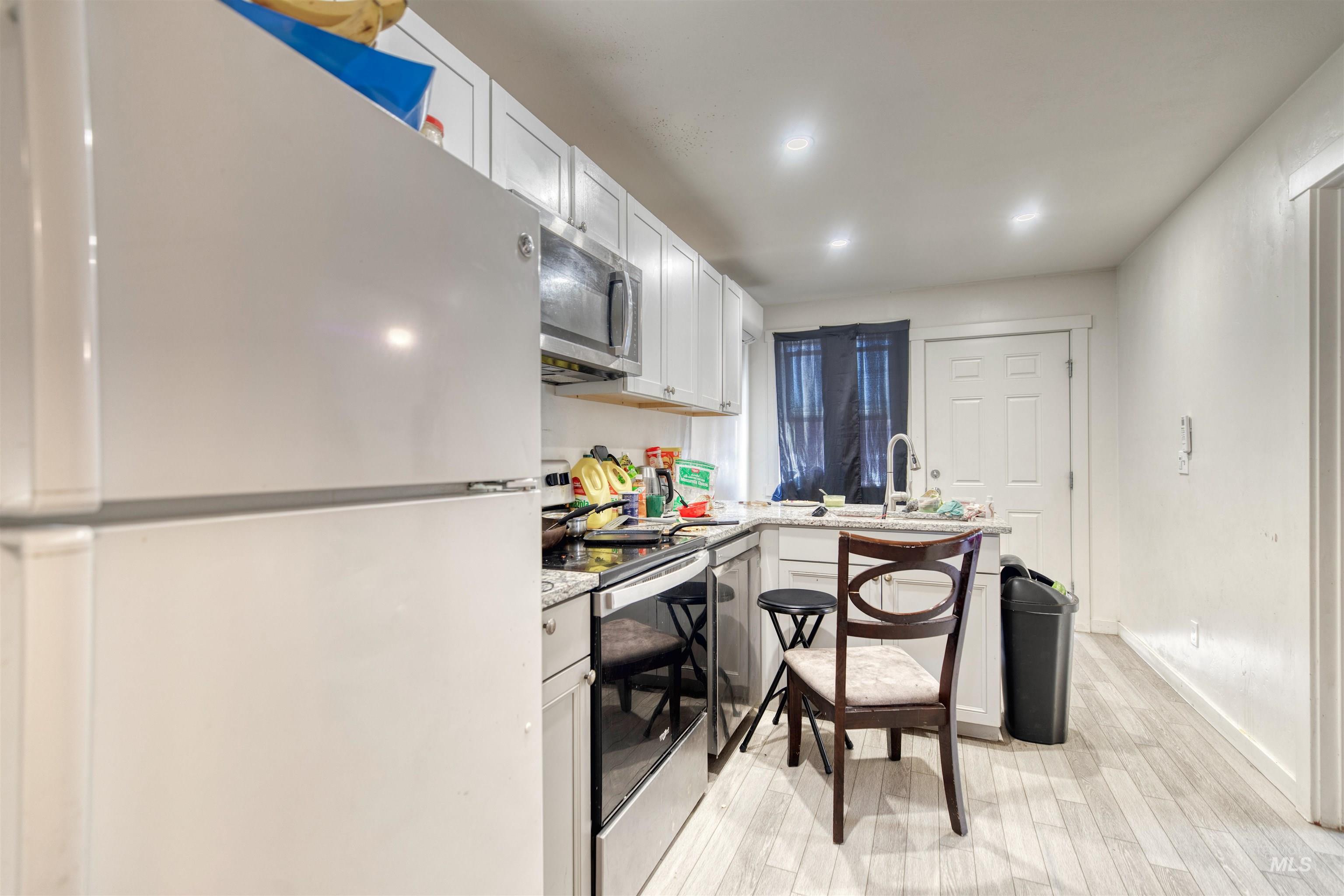 Kitchen featuring stainless steel appliances, light wood finished floors, white cabinets, a peninsula, and light stone countertops