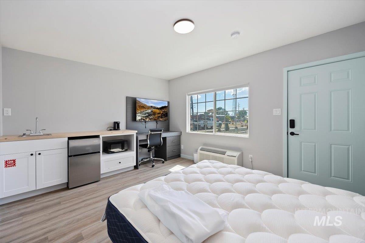 Bedroom with freestanding refrigerator, light wood-style floors, a wall mounted AC, and a desk