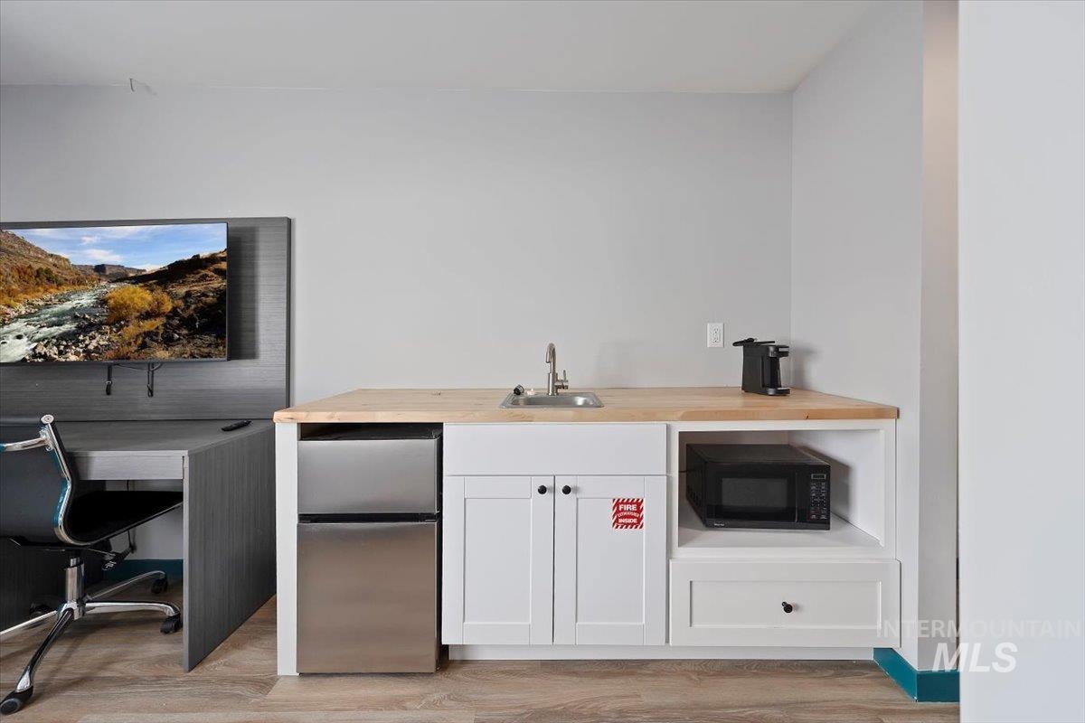 Bar area featuring freestanding refrigerator, black microwave, and light wood-style floors
