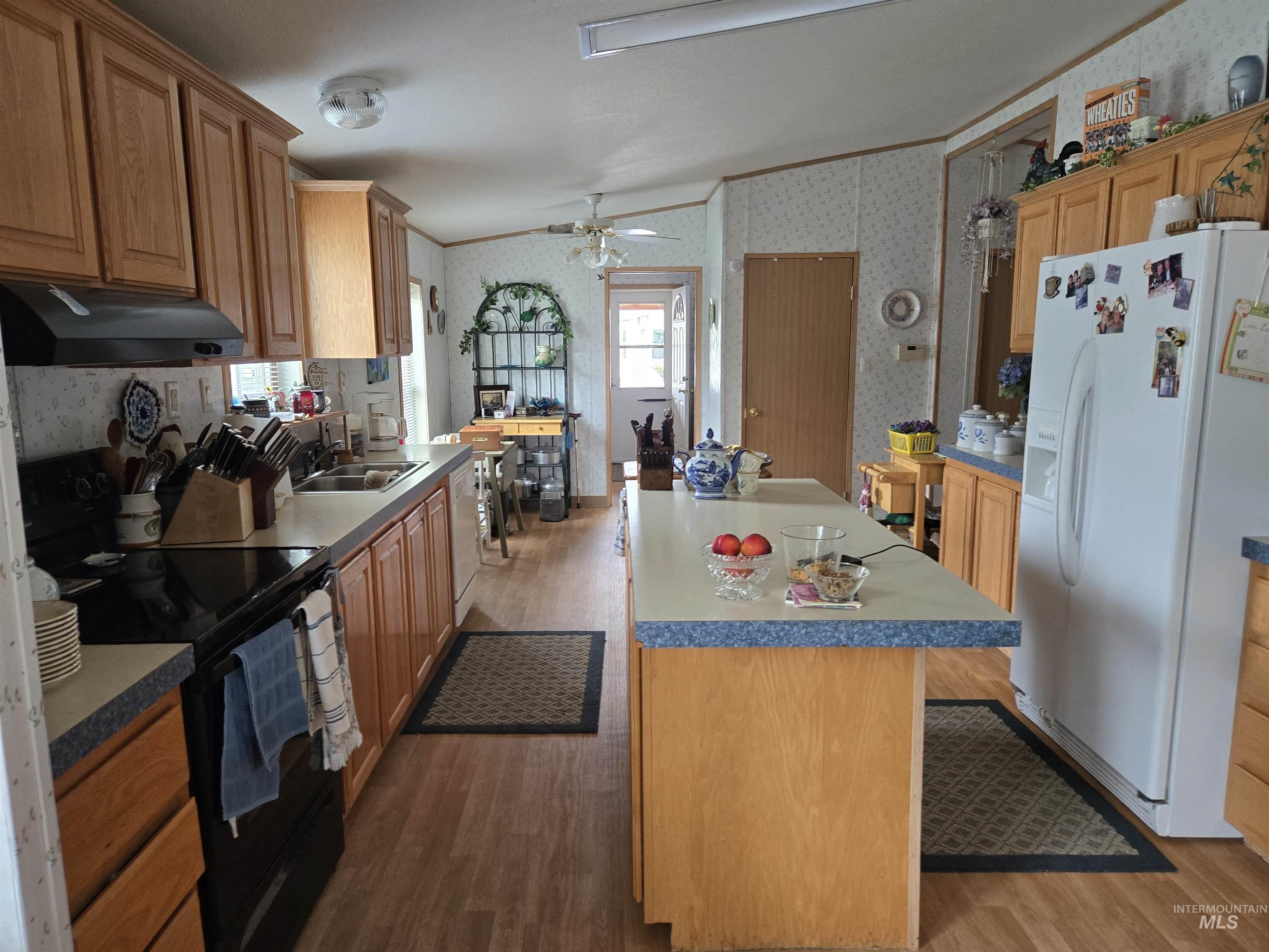Kitchen with wallpapered walls, white appliances, wood finished floors, a center island, and under cabinet range hood