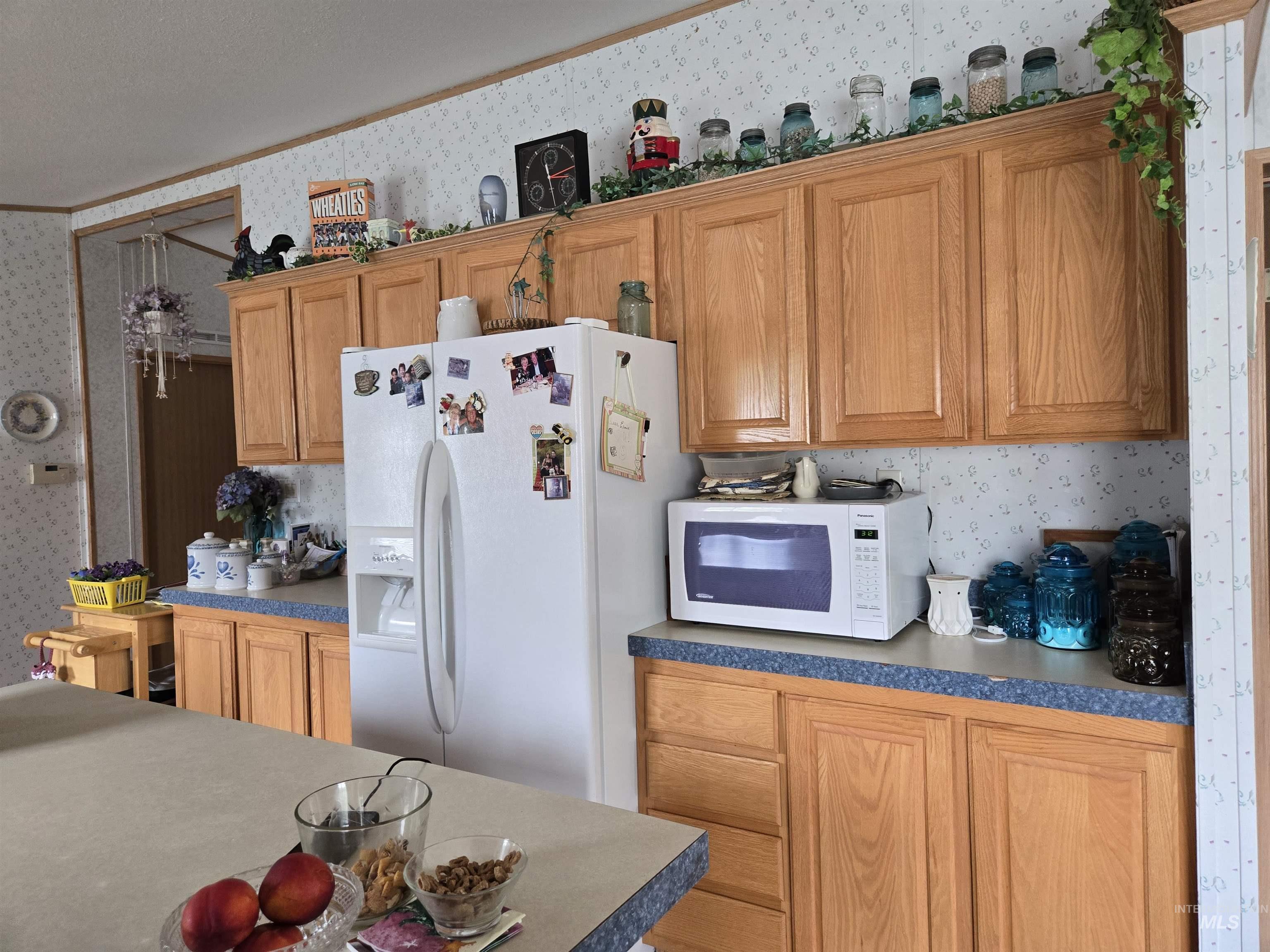 Kitchen with wallpapered walls, crown molding, white appliances, and dark countertops