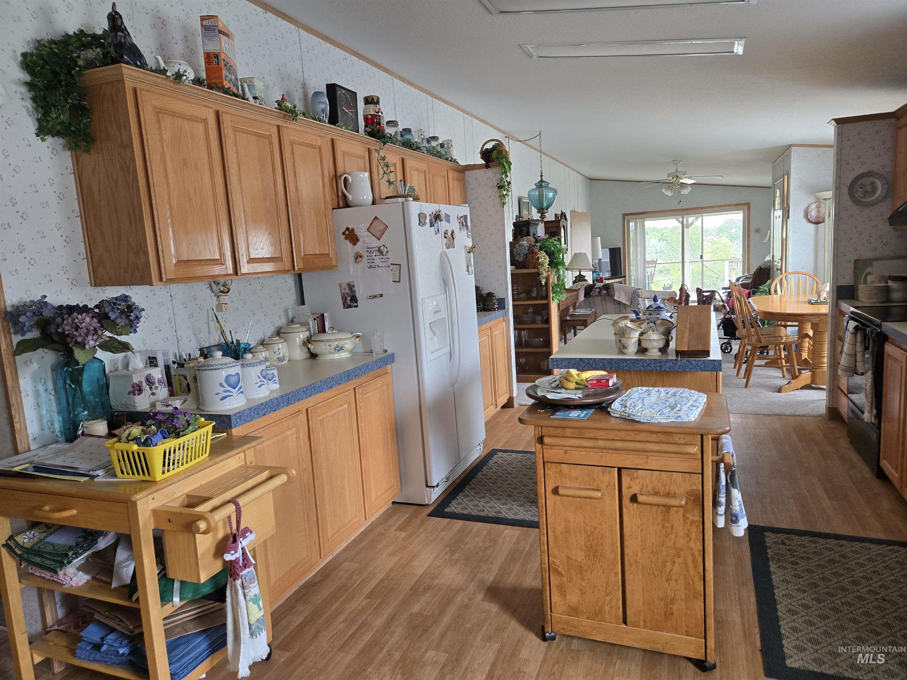 Kitchen with light wood-style floors, a kitchen island, wallpapered walls, white fridge with ice dispenser, and black range with electric stovetop