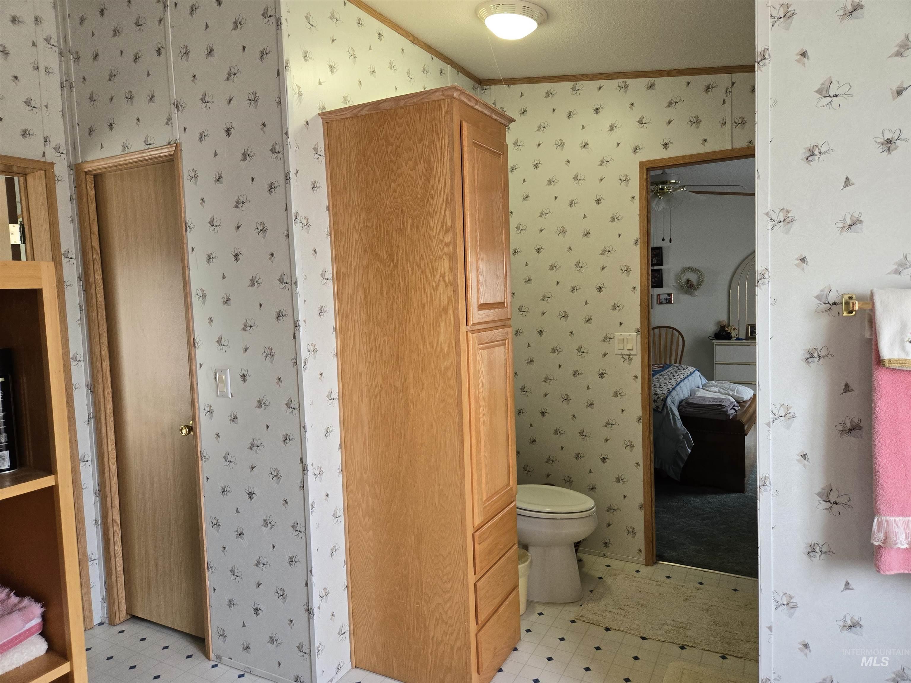 Ensuite bathroom featuring wallpapered walls, tile patterned floors, and ornamental molding