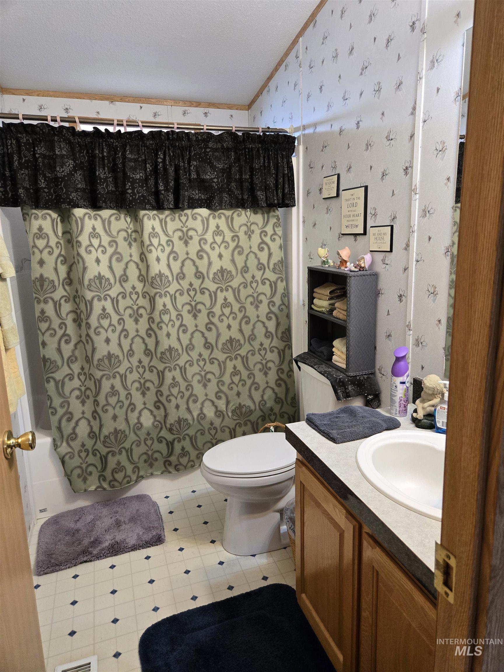 Bathroom featuring wallpapered walls, vanity, lofted ceiling, shower / tub combo with curtain, and ornamental molding