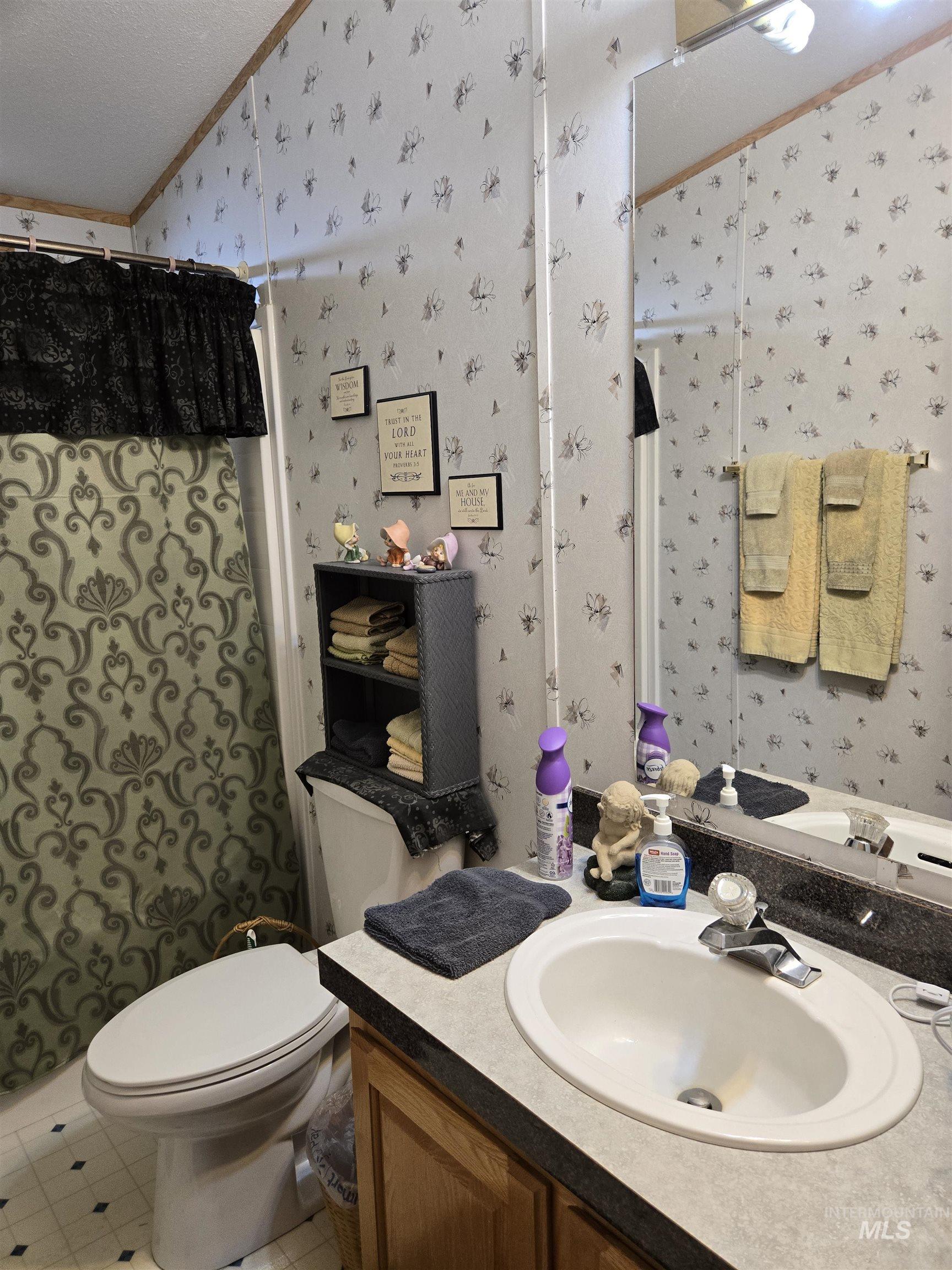 Bathroom featuring wallpapered walls, crown molding, vanity, a shower with shower curtain, and lofted ceiling