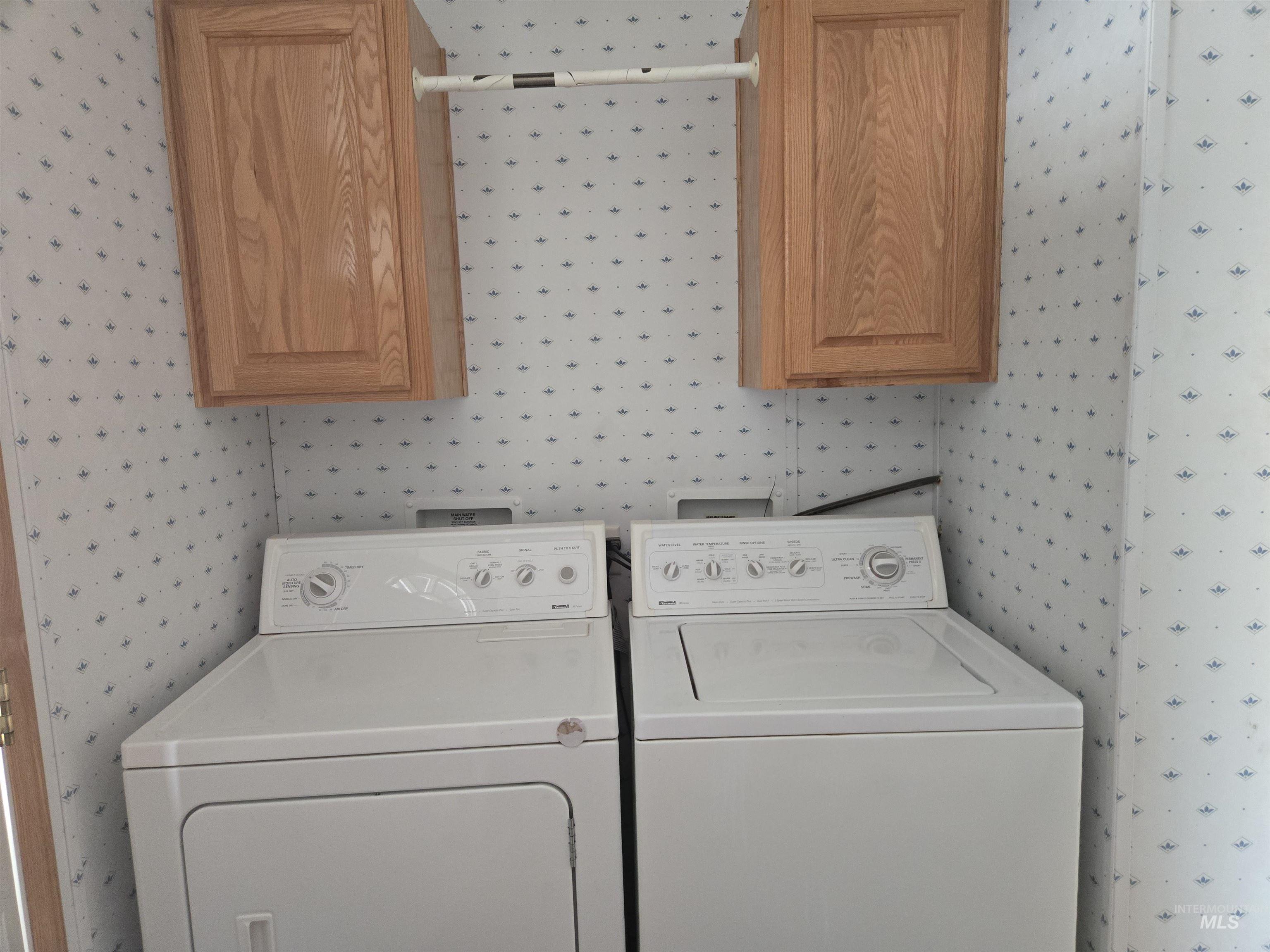 Laundry room with wallpapered walls, washer and dryer, and cabinet space