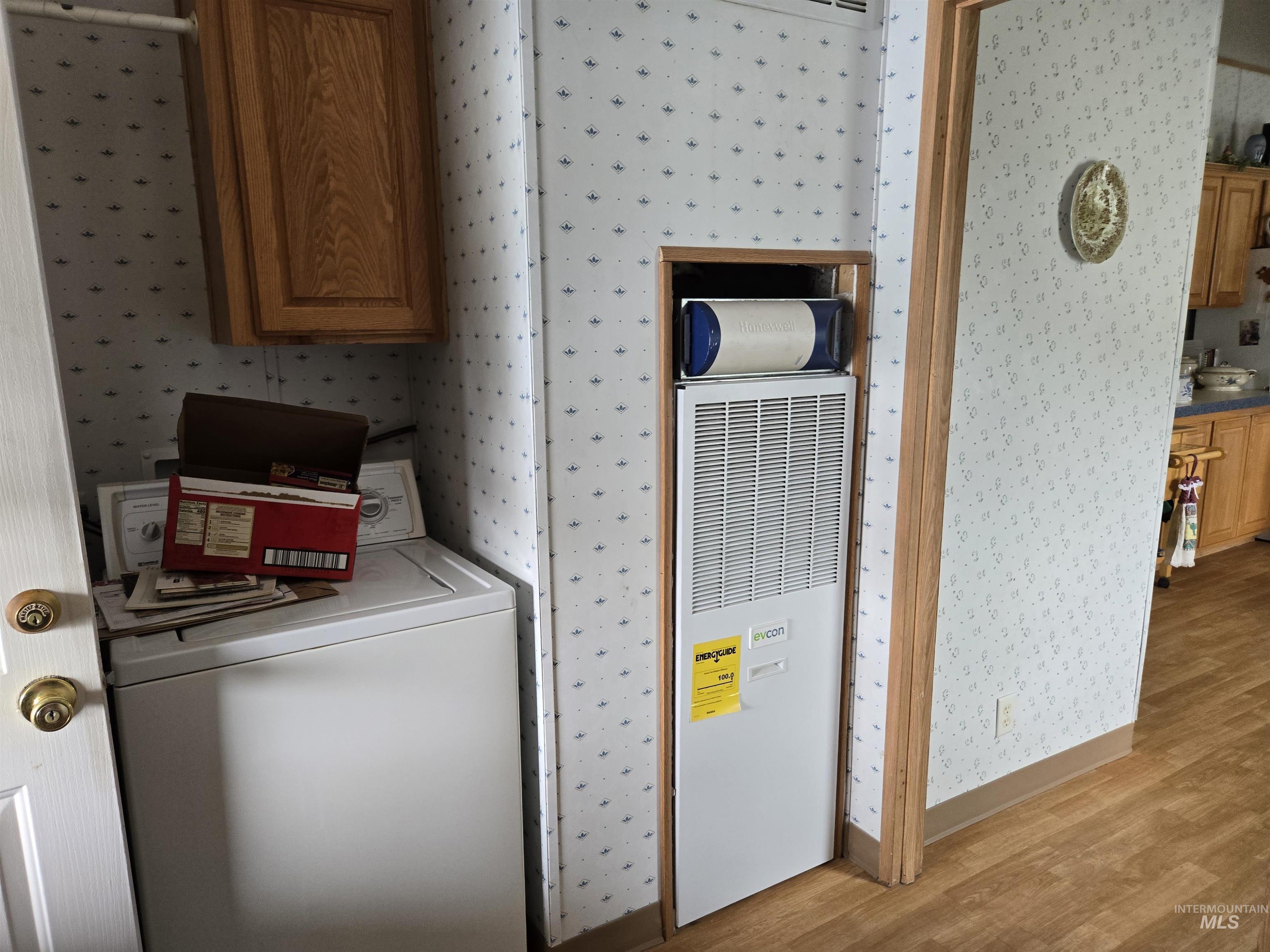 Washroom with wallpapered walls, washer / dryer, light wood finished floors, and a heating unit