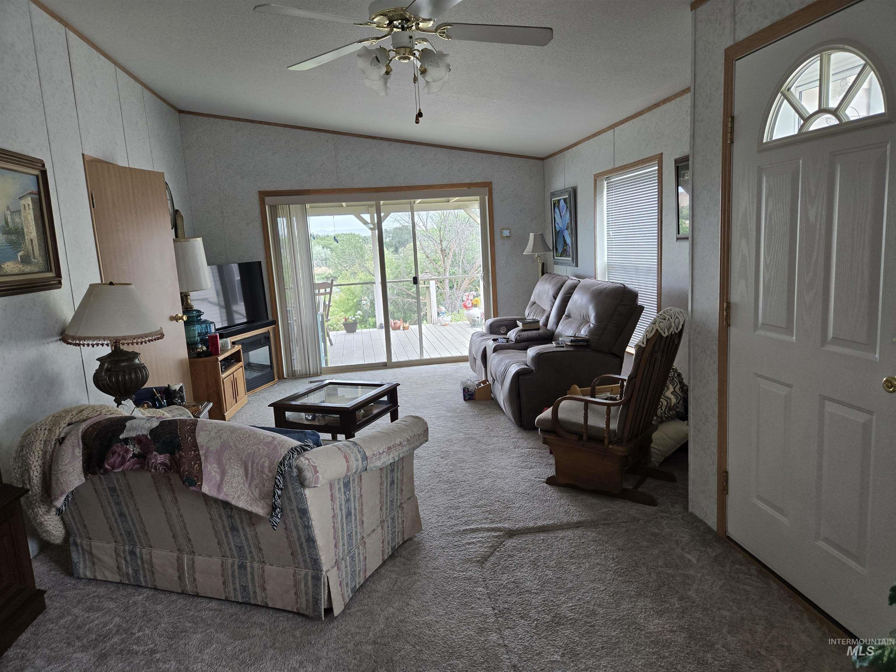 Carpeted living room featuring lofted ceiling, ceiling fan, and ornamental molding