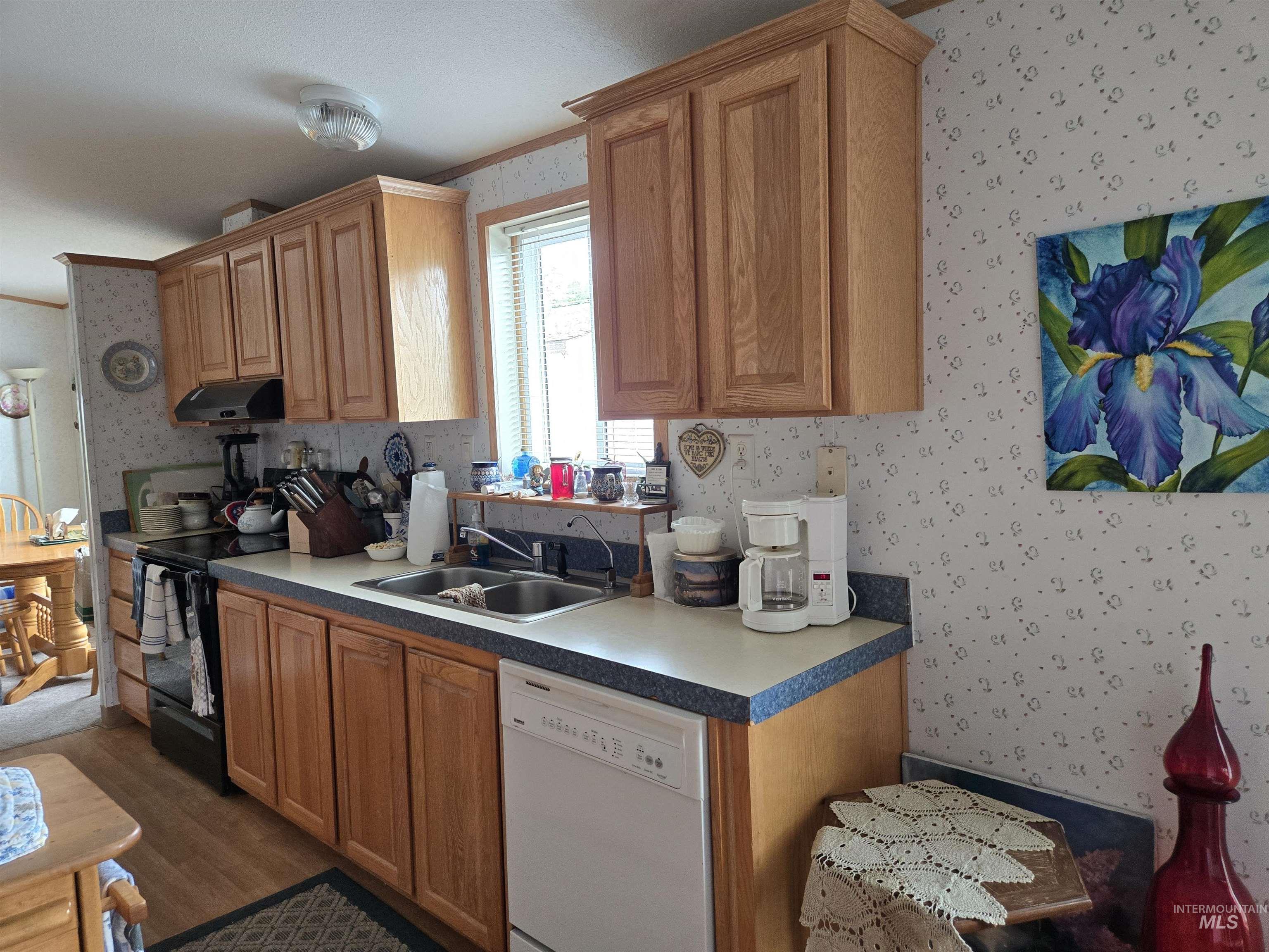 Kitchen with wallpapered walls, dishwasher, under cabinet range hood, and wood finished floors