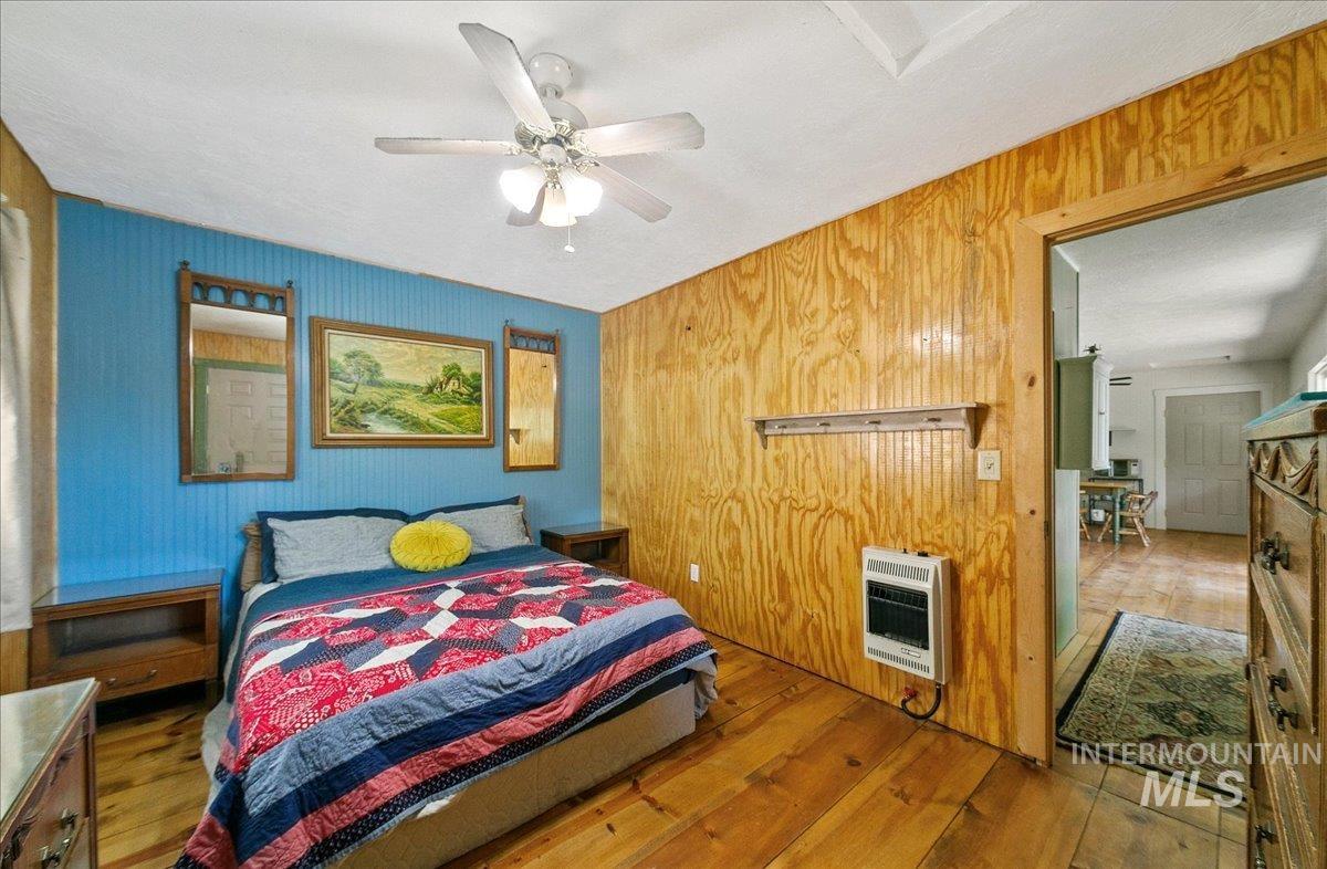 Bedroom with heating unit, wood finished floors, wood walls, and a ceiling fan