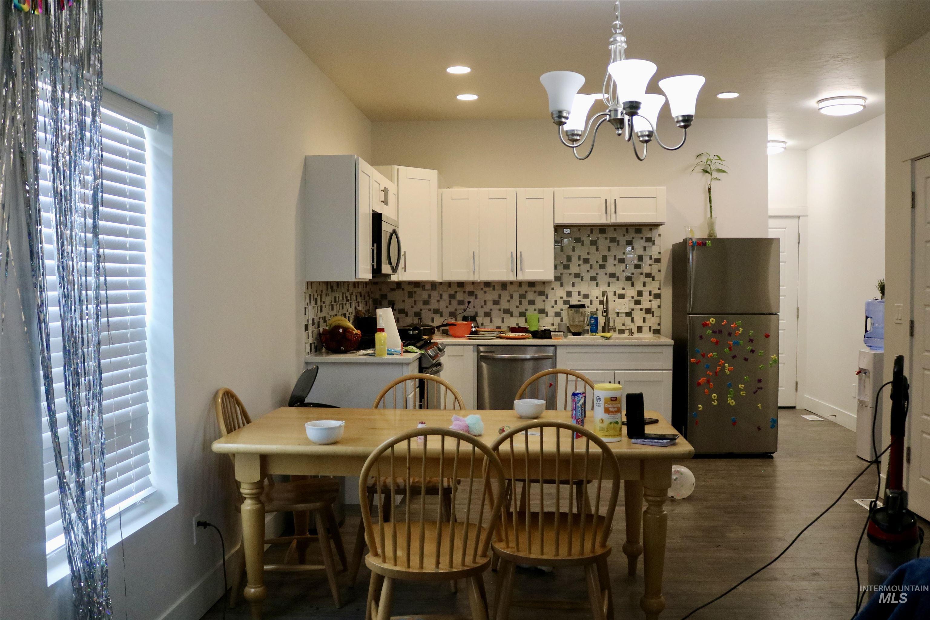 Kitchen featuring stainless steel appliances, a chandelier, tasteful backsplash, dark wood-style flooring, and hanging light fixtures