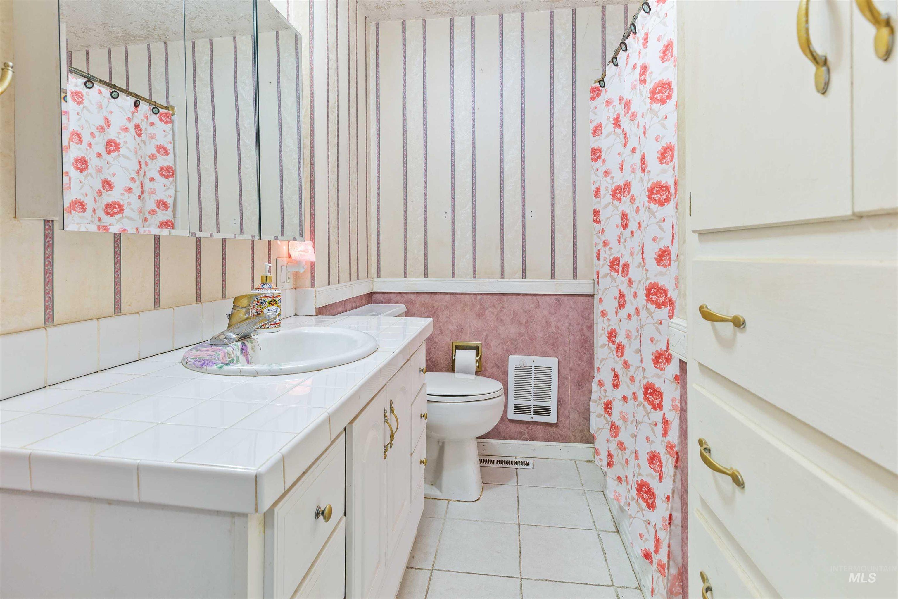 Bathroom with wallpapered walls, vanity, and tile patterned floors