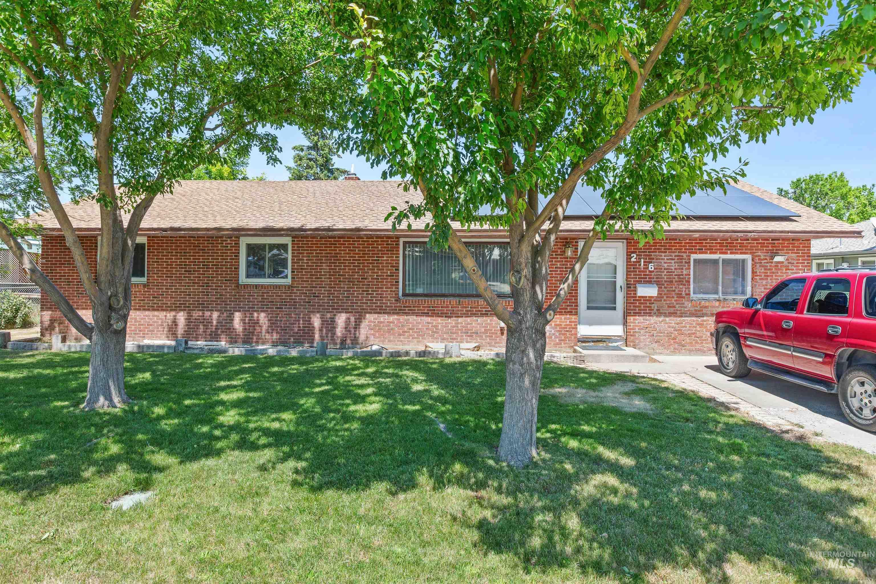 Ranch-style house with brick siding, solar panels, a front lawn, and a shingled roof