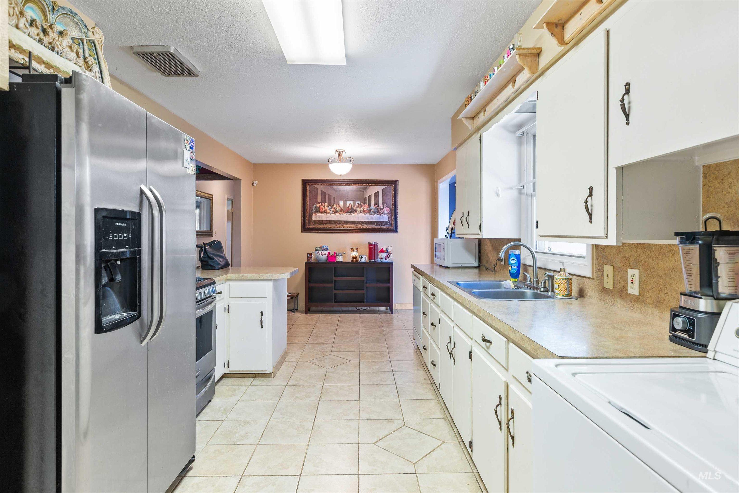 Kitchen featuring stainless steel appliances, washer / dryer, light countertops, white cabinets, and light tile patterned floors