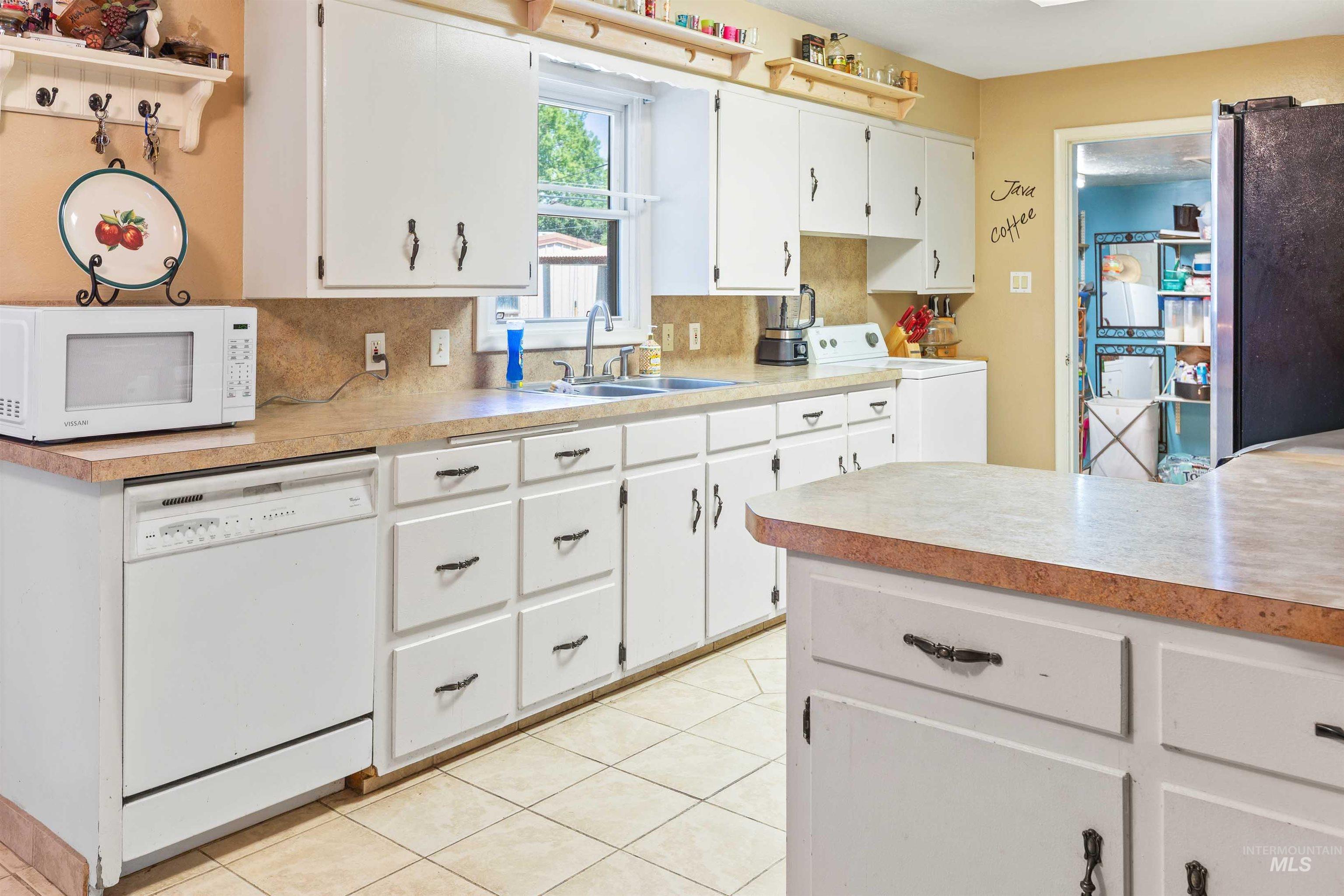 Kitchen with white appliances, washer / dryer, white cabinets, light countertops, and light tile patterned floors