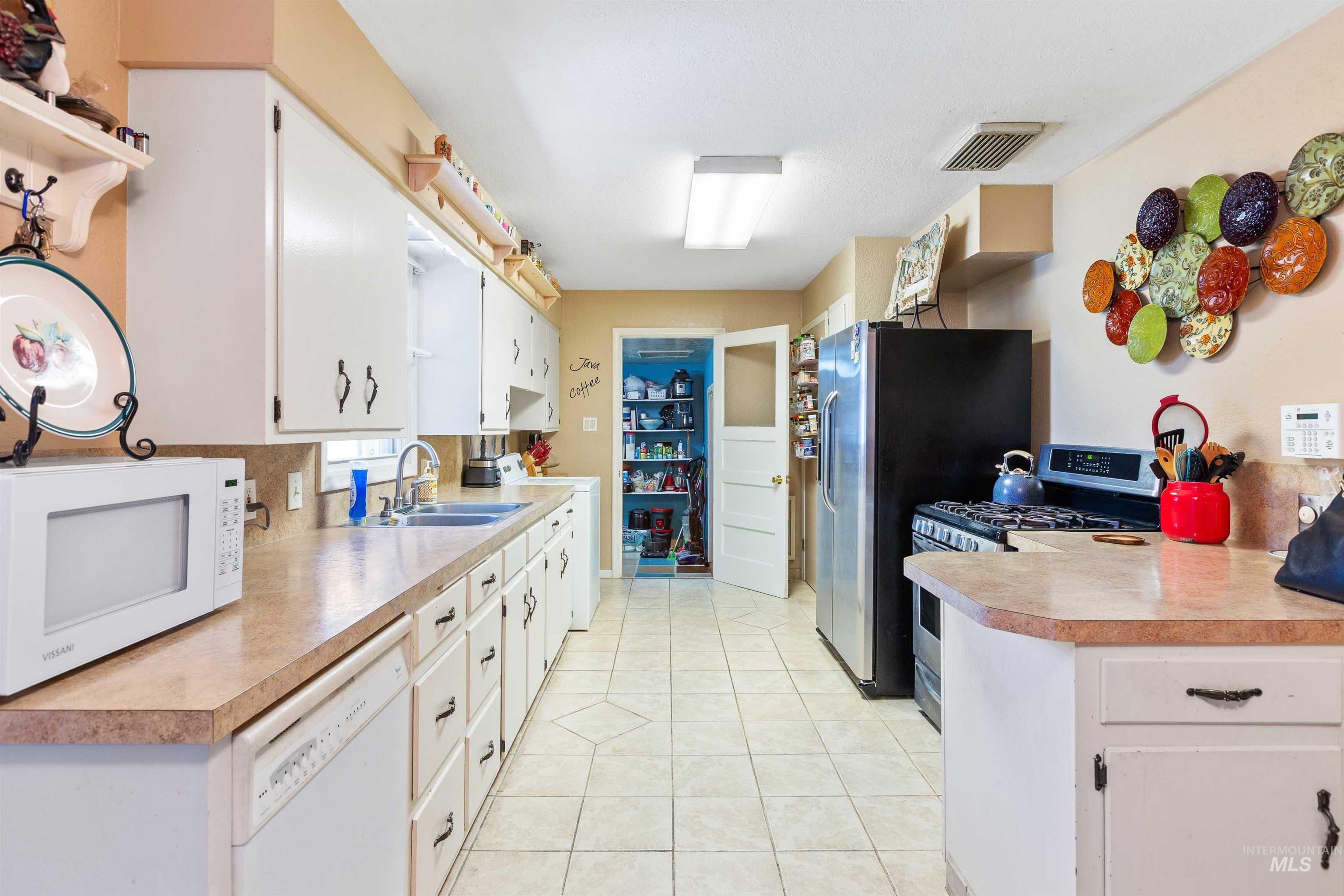 Kitchen with stainless steel appliances, washer / clothes dryer, light countertops, white cabinets, and light tile patterned flooring
