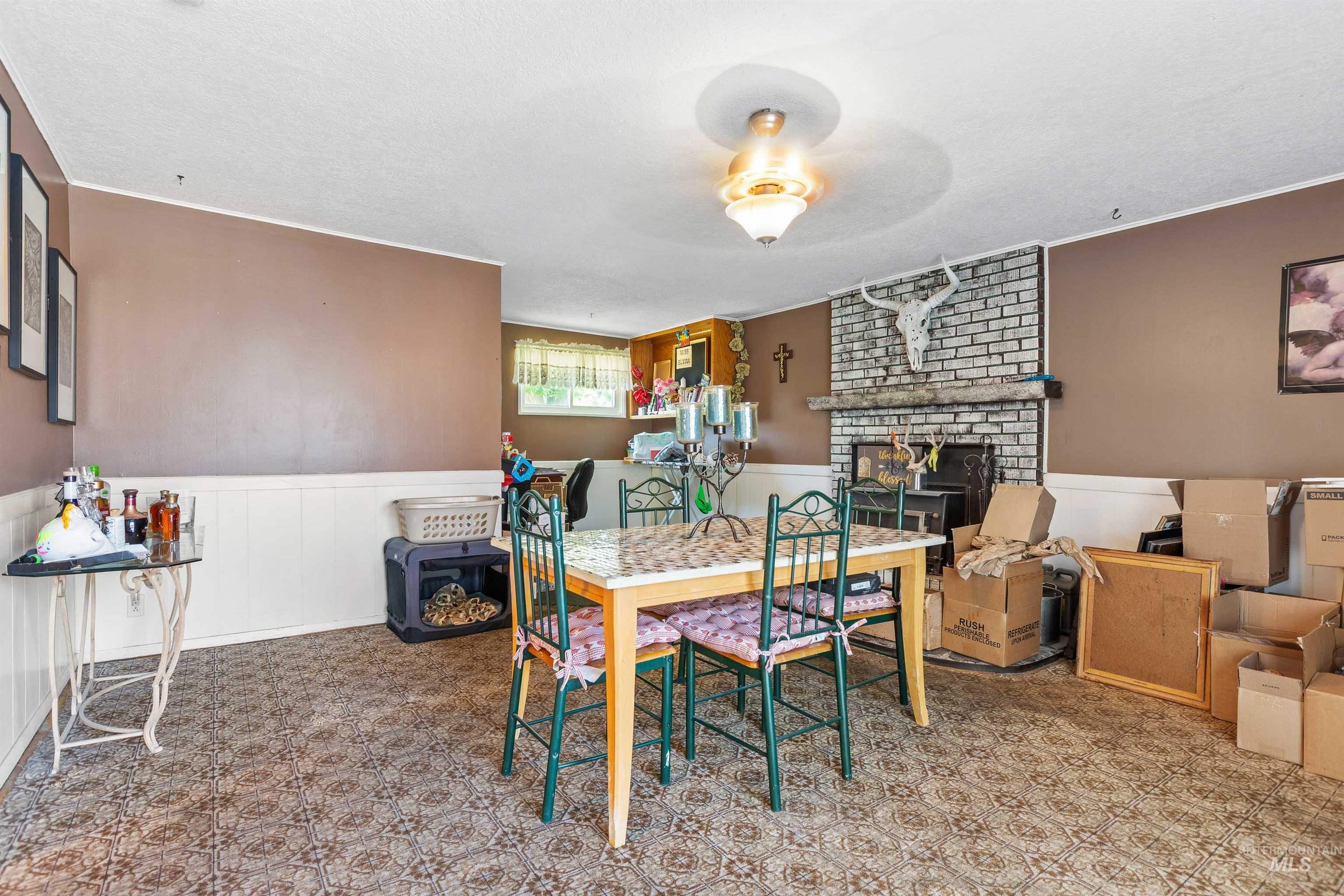 Dining space with tile patterned floors, a brick fireplace, a wainscoted wall, and a textured ceiling