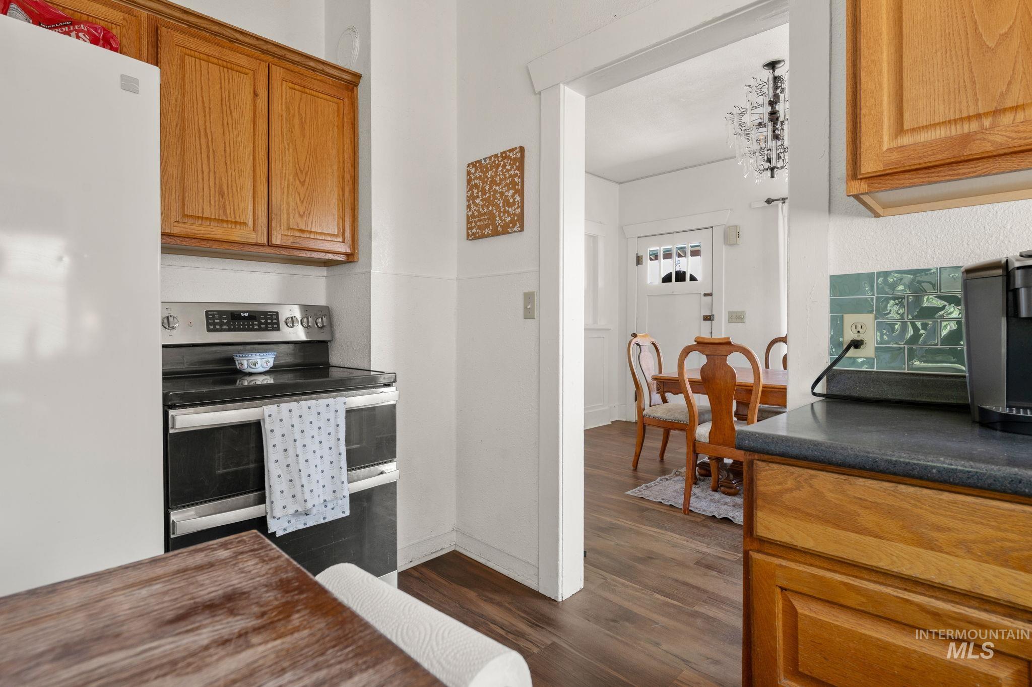 Kitchen with electric stove, freestanding refrigerator, dark wood finished floors, dark countertops, and brown cabinets