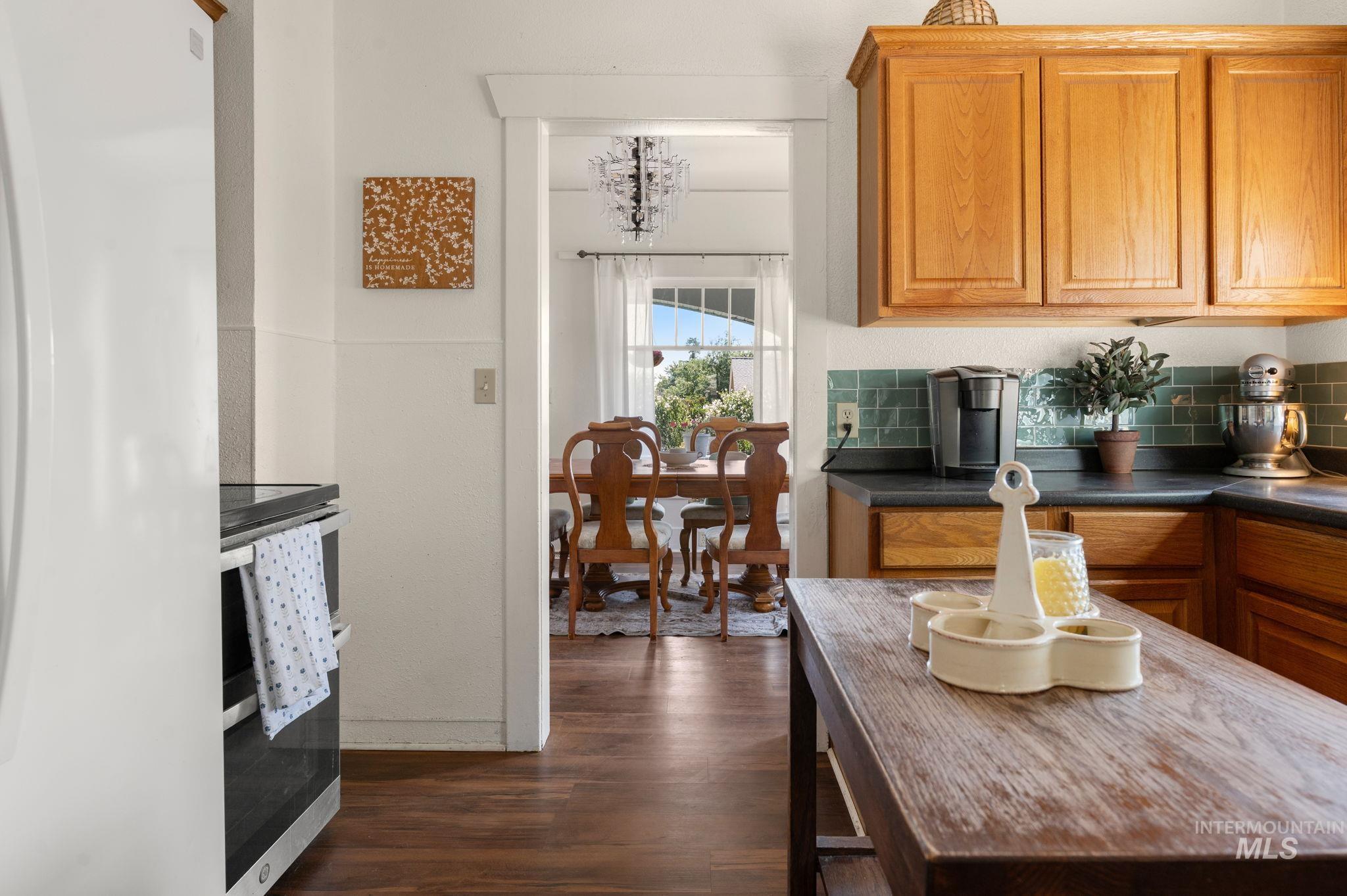 Kitchen with stove, backsplash, dark wood-type flooring, freestanding refrigerator, and dark countertops