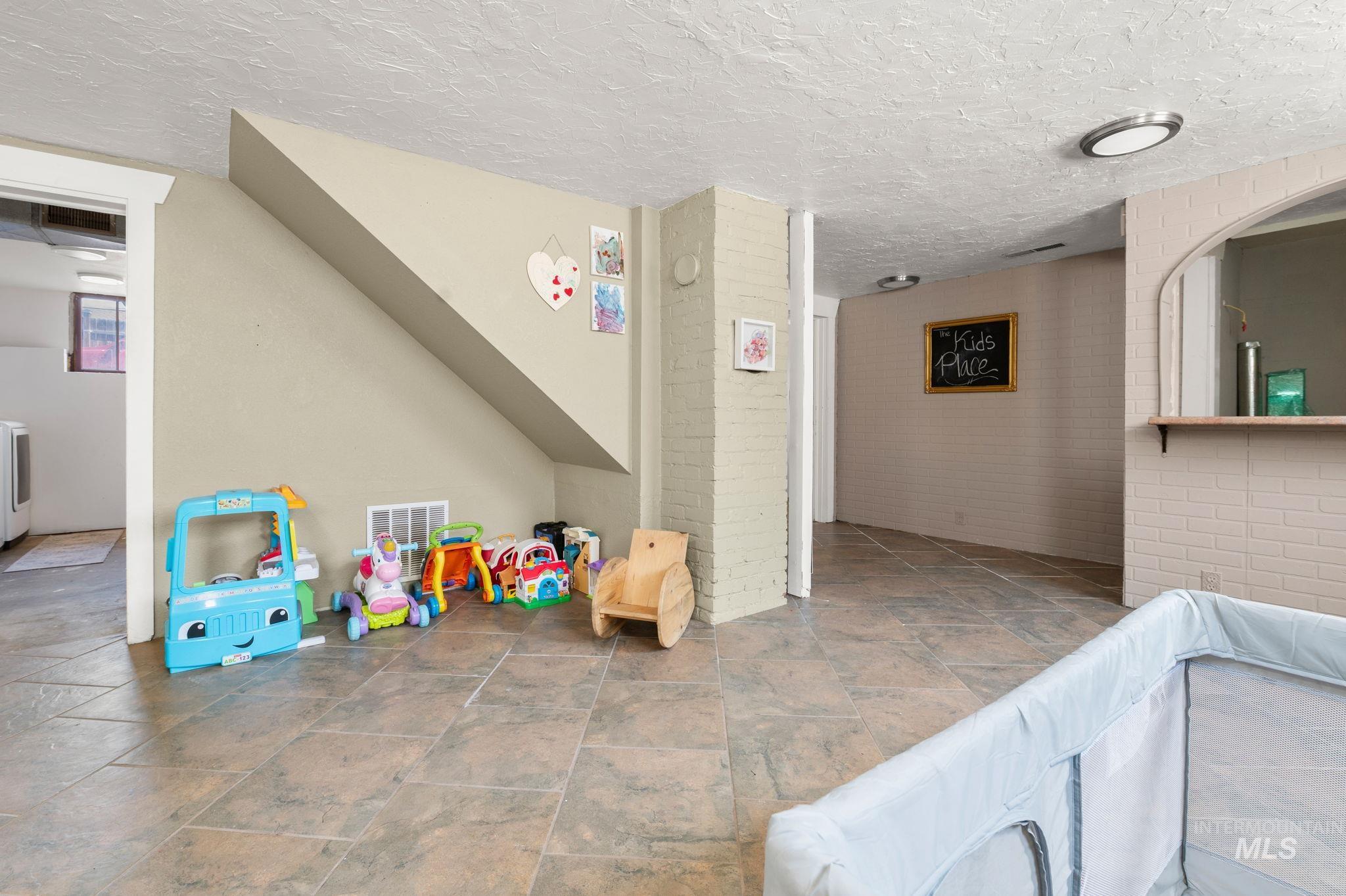 Recreation room with brick wall, stone finish flooring, and a textured ceiling