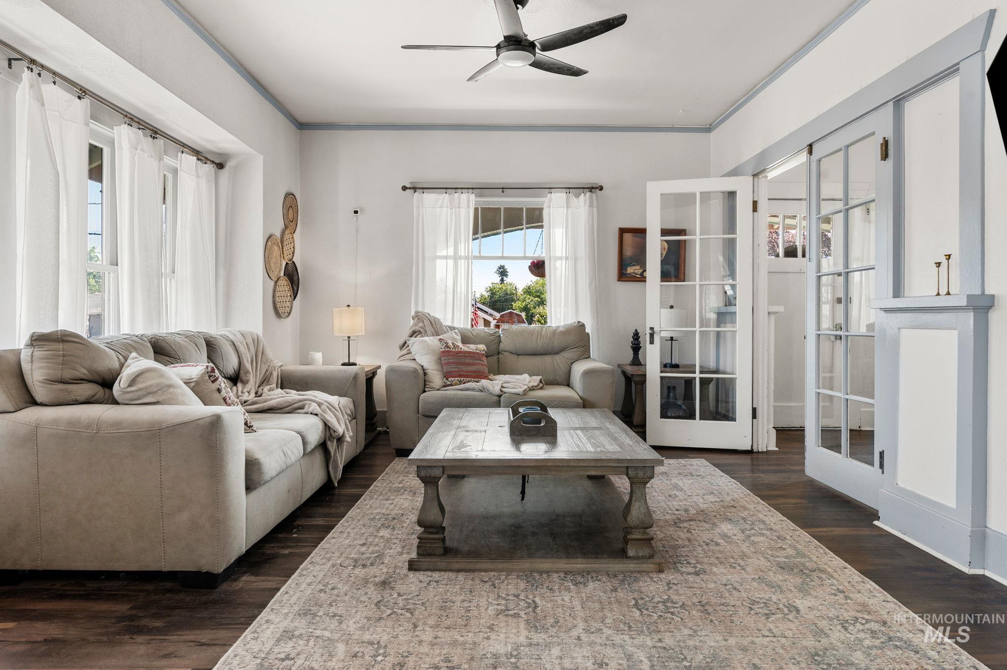 Living area featuring a ceiling fan, french doors, dark wood-type flooring, and ornamental molding