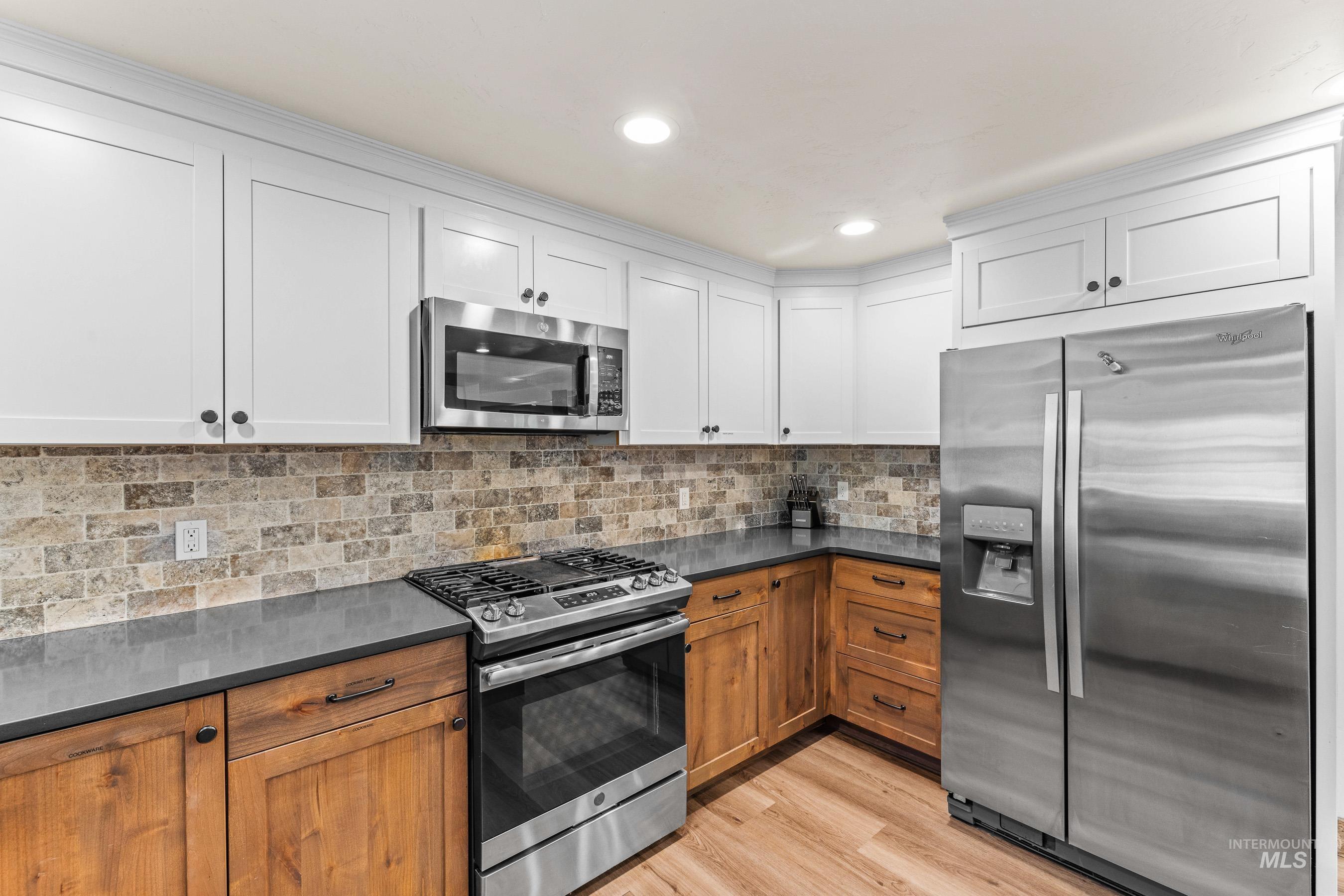 Kitchen featuring appliances with stainless steel finishes, dark countertops, light wood-type flooring, and decorative backsplash